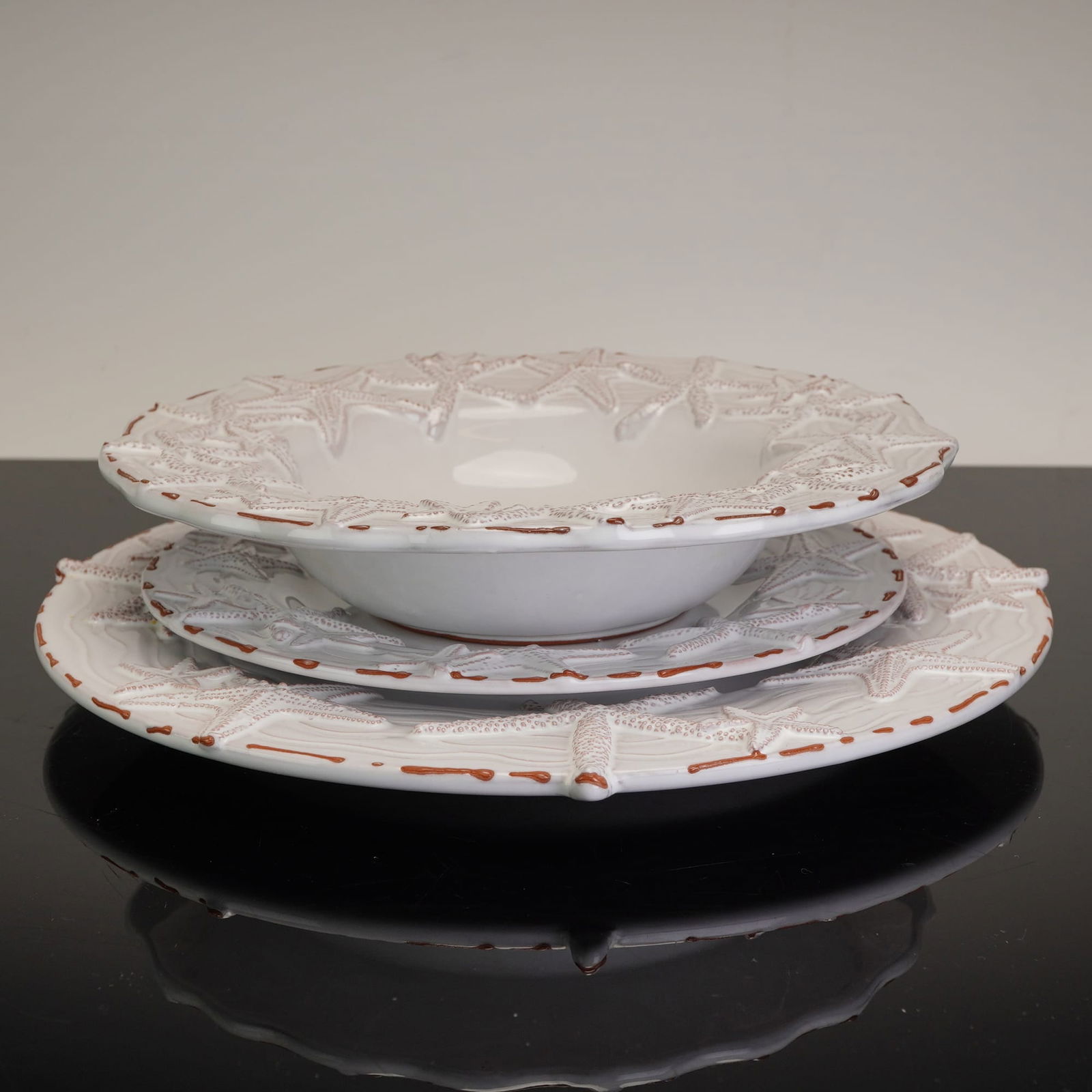 Mud Pie Starfish Three-Piece Place Setting: A three-piece ceramic place setting by Mud Pie in the Starfish pattern. This contemporary set is crafted from glazed earthenware and includes one dinner plate, one dessert plate, and one soup bowl. Th