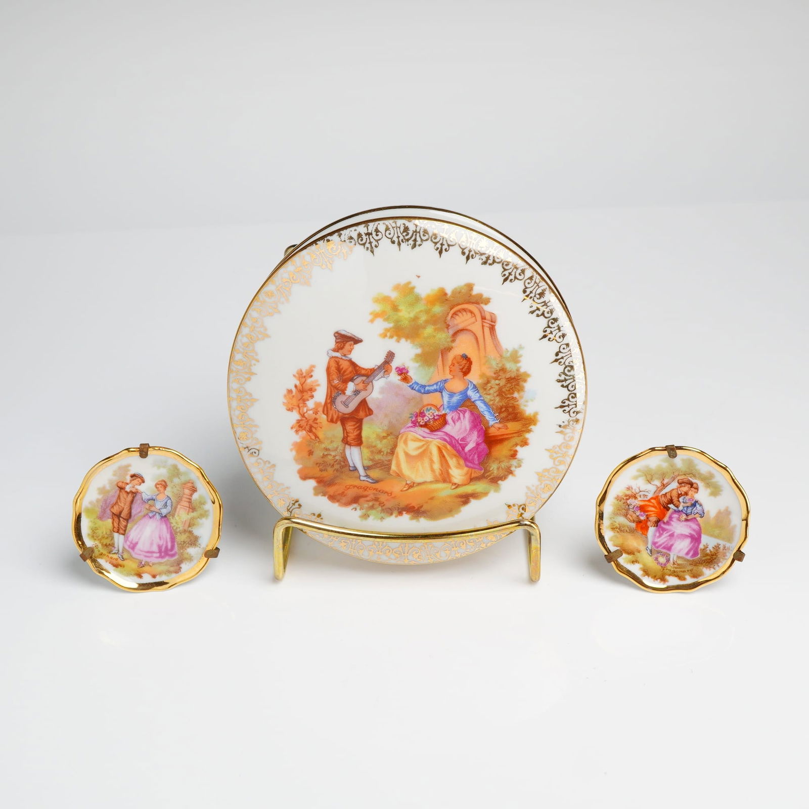 3pc Limoges France Porcelain Decorative Items in the Fragonard Style: A three-piece collection of Limoges France porcelain decorative items, comprising one large round lidded box and a pair of miniature scalloped display plates. All pieces feature transfer-printed decor