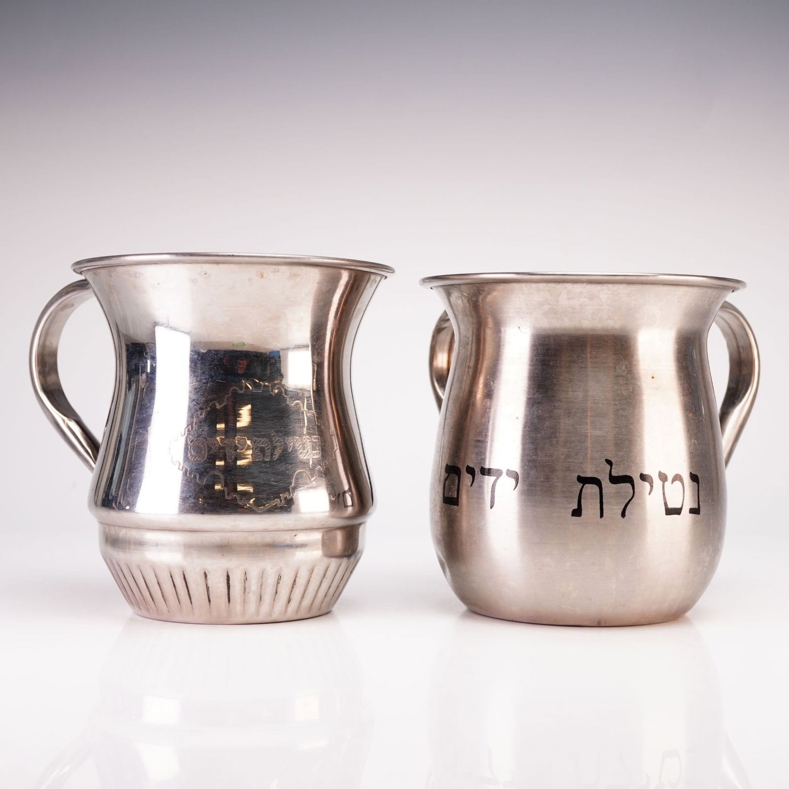 Modern Stainless Steel Judaica Ritual Washing Cups, Late 20th/Early 21st Century: A pair of silver toned double handled pitchers for ritual washing, used for the Jewish observance of Netilat Yadayim (Washing of Hands). These utilitarian vessels, often referred to as natlas, are con