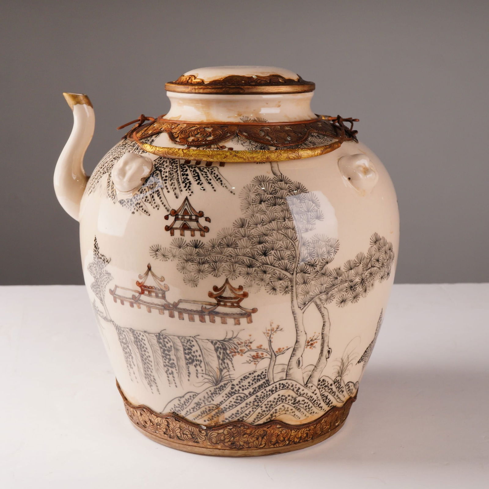 Large Gilt-Mounted Ceramic Lidded Kettle with Asian Landscape: A large, cylindrical ceramic kettle and its matching cover that features a creamy white glaze adorned with monochrome black and gray decorations depicting an Asian waterside and mountainous landscape.