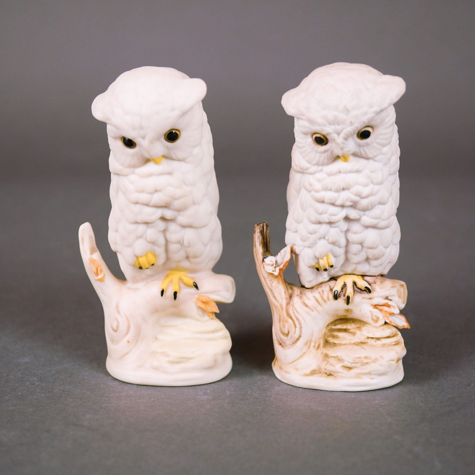 Cybis Porcelain Baby Snowy Owl Figurines, Model 334: A pair of Cybis matte bisque porcelain figurines depicting baby owls, also known as Snowy Owls, perched on gnarled tree stumps. These mid-century pieces feature detailed plumage, yellow-painted eyes,