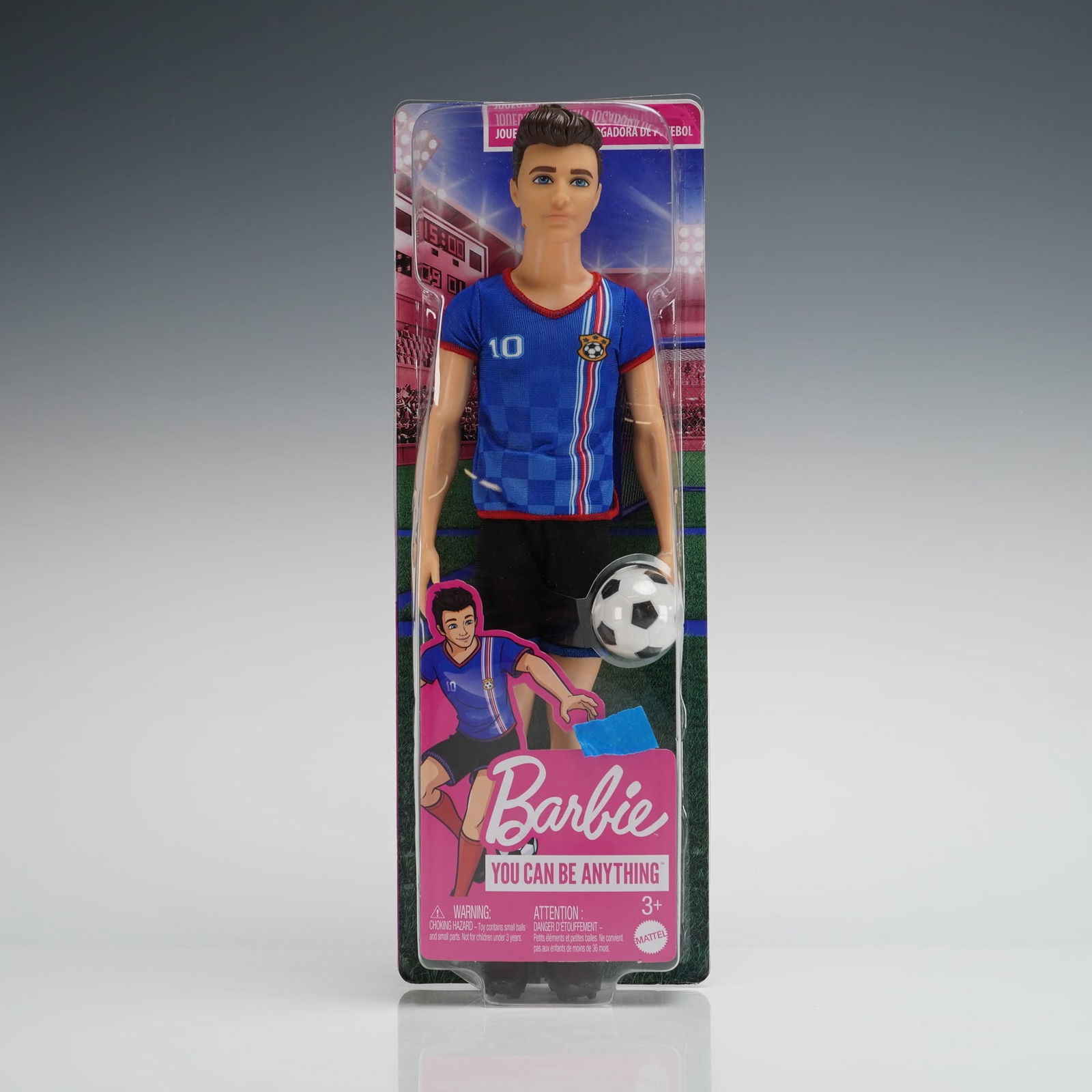 Mattel Barbie You Can Be Anything Soccer Player Doll: The plastic doll is sealed in its original cardboard and clear plastic blister packaging. The figure wears a blue jersey numbered "10," black shorts, and red socks, and holds a small plastic soccer ba
