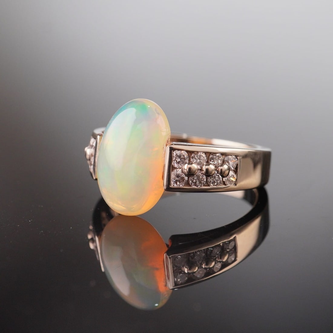 14K Gold 3.39ct Opal and Diamond Ring: A yellow gold ring featuring an oval-shaped opal, shouldered by eight round brilliant cut diamonds on each side, totaling sixteen diamonds. The band is marked US. Tested with Thermo Scientific Niton X