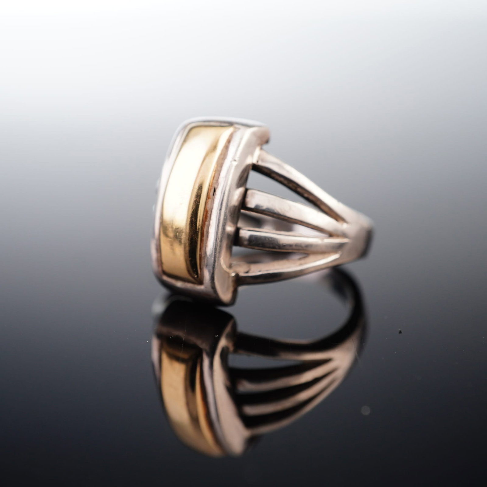 18K Yellow Gold and Sterling Silver Mixed Metal Ring: This contemporary mixed metal cocktail ring features a bold architectural design. The piece is crafted with a sterling silver body and a prominent 18K yellow gold central inlay. The centerpiece consis