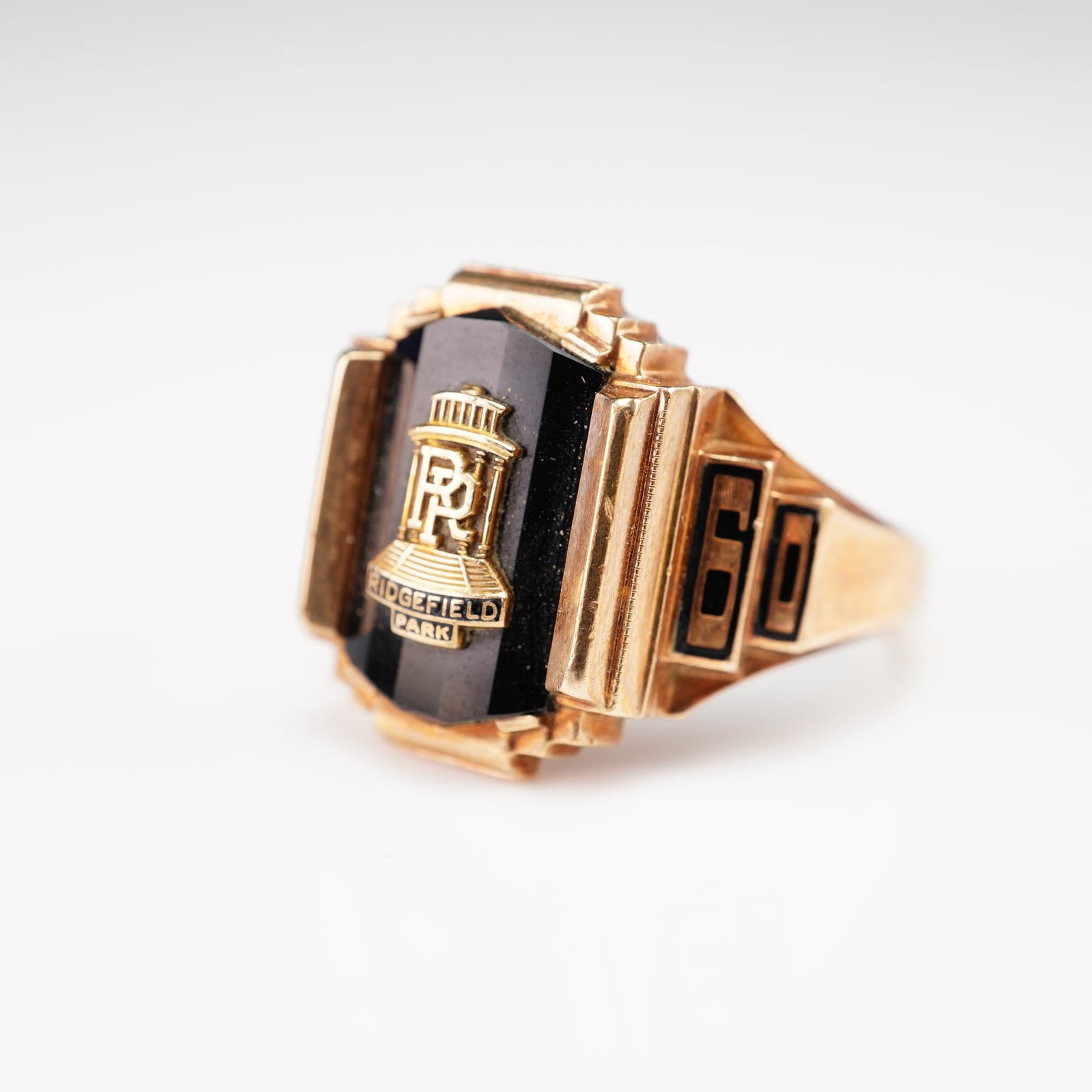 10K Gold Jostens 1960 Ridgefield Park Class Ring with Onyx: This vintage 10k yellow gold Jostens 1960 Ridgefield Park class ring features a rectangular, faceted-top black onyx plaque. The onyx is set with an applied 10k yellow gold school emblem for Ridgefield