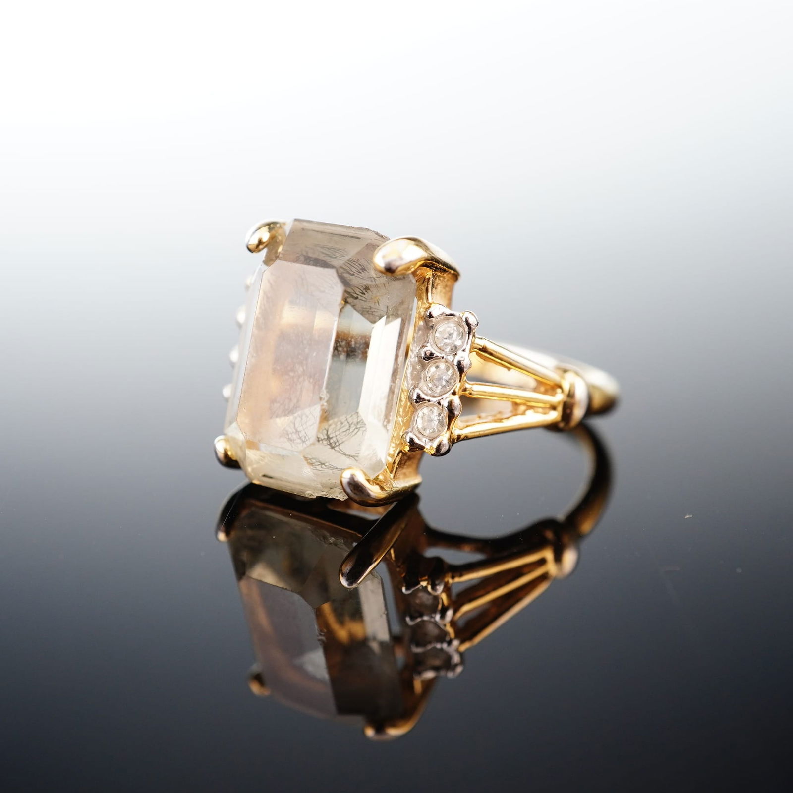 Joseph Esposito 14KT Gold Electroplate Emerald-Cut Gray Stone Ring: A cocktail ring featuring 14KT gold electroplate construction by designer Joseph Esposito. The centerpiece is a large emerald-cut gray hued stone shouldered by three clear round accent stones on each