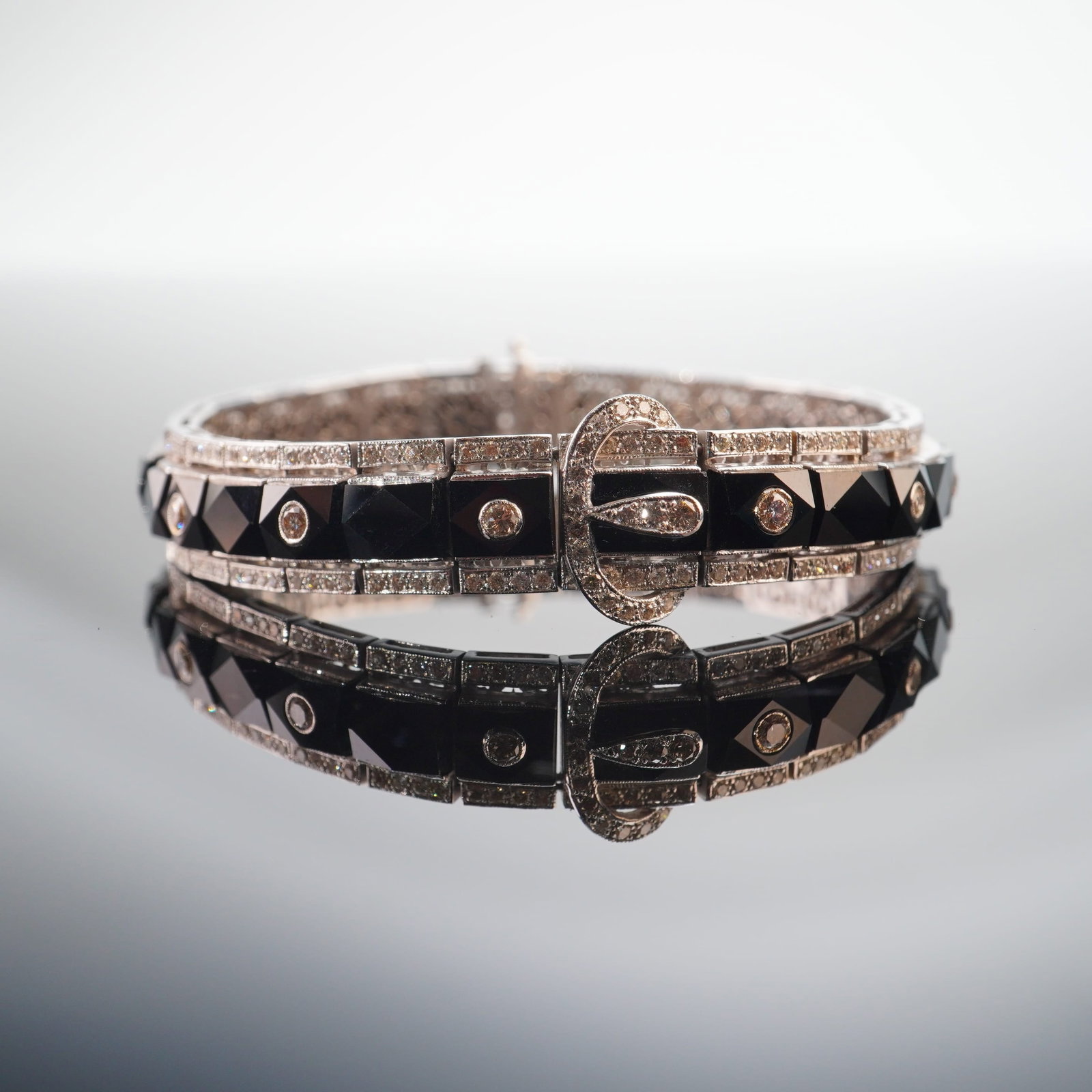 16K White Gold, Diamond & Onyx Art Deco Buckle Style Bracelet: Crafted from 16K white gold, this elegant Art Deco buckle style line bracelet features geometric symmetry with French-cut black onyx stones and round cut diamonds. Stamped inside the clasp. Tested wit