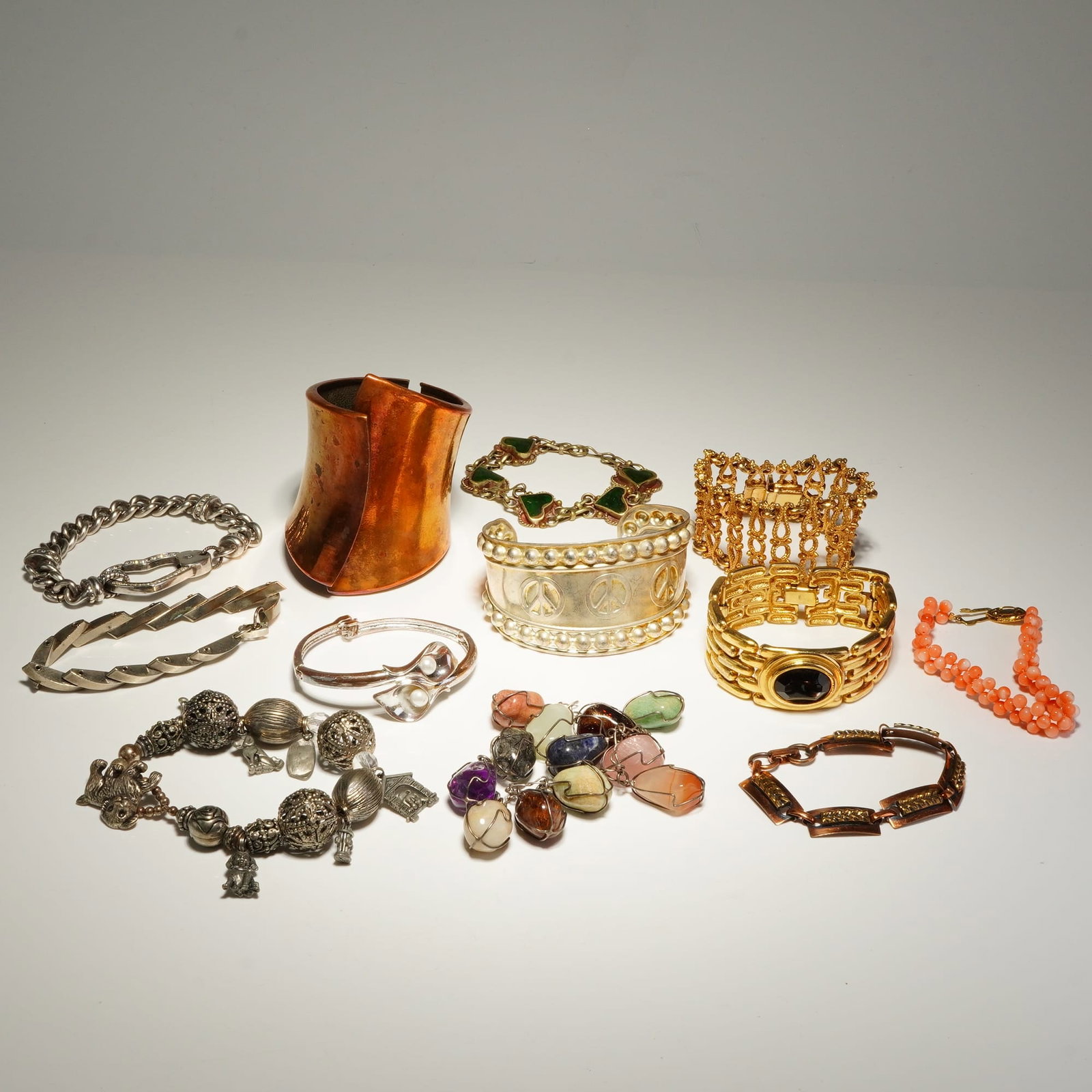 Assorted Multi-Tone Base Metal Costume Jewelry Bracelets: This collection features an assortment of costume jewelry in silver-tone, gold-tone, and copper-tone base metals. The lot contains a wide gold-tone link bracelet centering a large oval black cabochon,