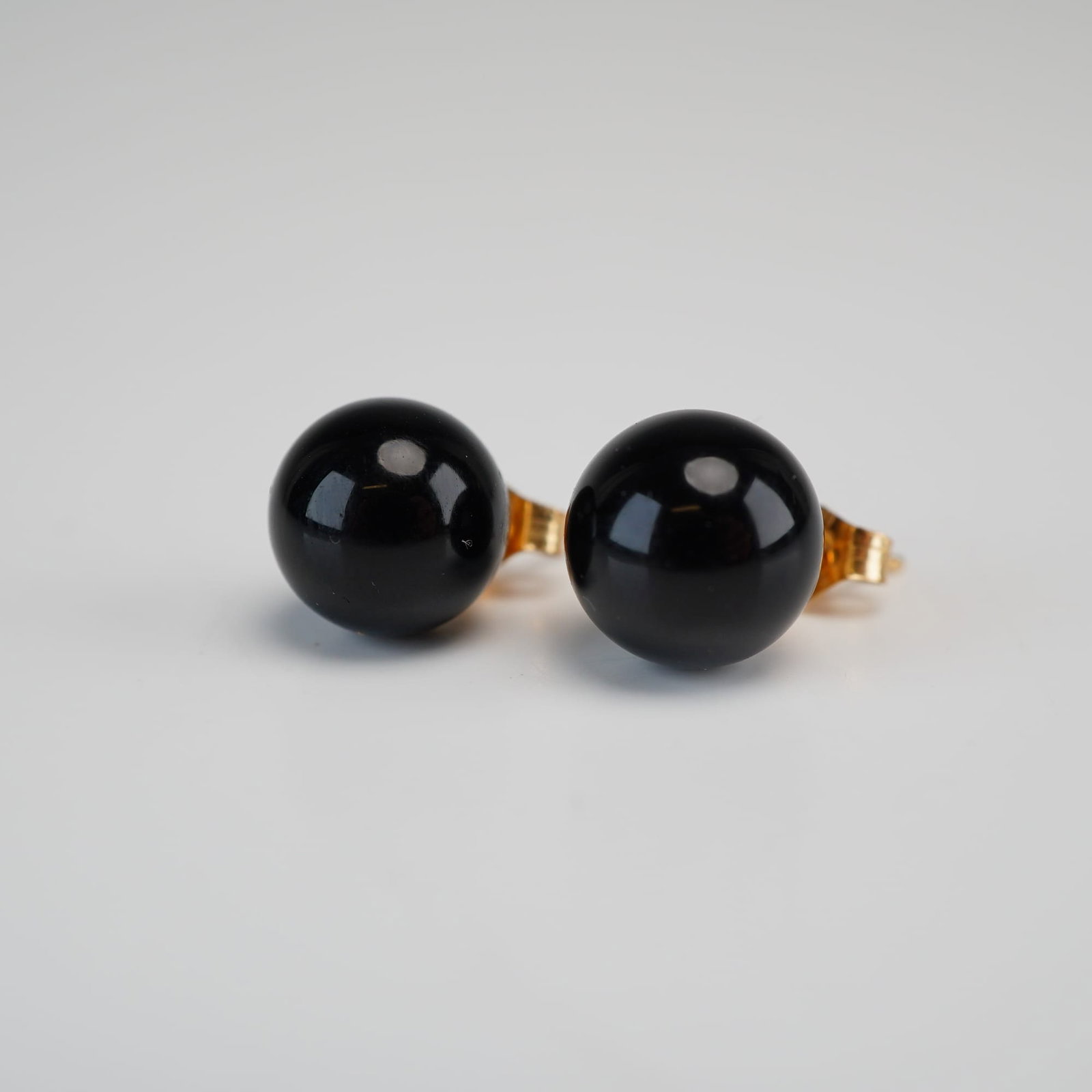 14K Yellow Gold Black Onyx Stone Ball Stud Earrings: This pair of stud earrings is crafted in 14K yellow gold and features spherical black onyx beads. Each onyx bead is mounted on a gold post. The earrings are secured with matching butterfly friction ba