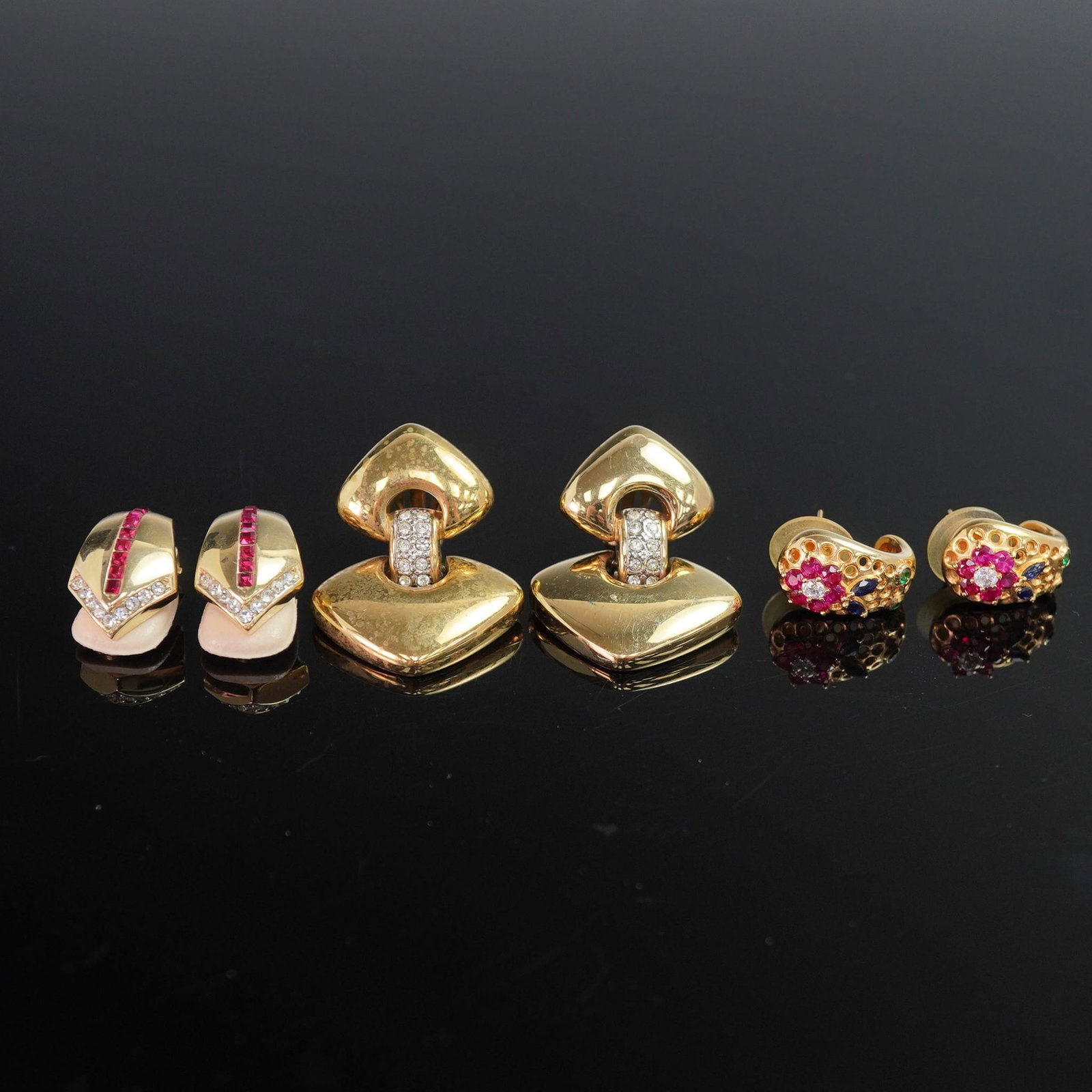3 Pairs Gold-Tone Earrings with Floral and Geometric Designs: A vibrant trio of gold-tone earrings showcasing bold shapes and sparkling details, with a mix of closures. The first pair, marked 18KGP, features a vivid magenta floral motif with faceted petals surro