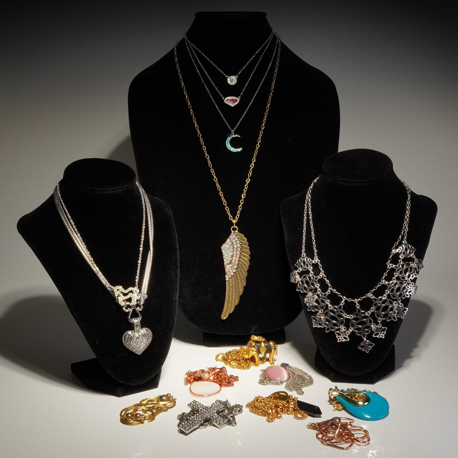 Assorted Gold-Tone and Silver-Tone Costume Jewelry Necklaces: This collection of fashion jewelry comprises various necklaces in silver, yellow gold, and rose gold-toned base metals. Notable pieces include a large yellow gold-tone angel wing pendant featuring pav