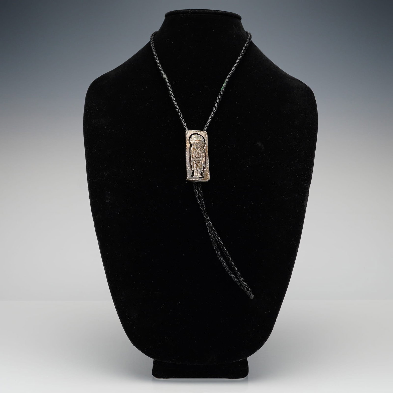 Navajo Sterling Silver Sunface Kachina Bolo Tie: This Navajo sterling silver bolo tie features a rectangular slide crafted in a traditional overlay style. The central design depicts a stylized kachina figure, characterized by a radial headdress and