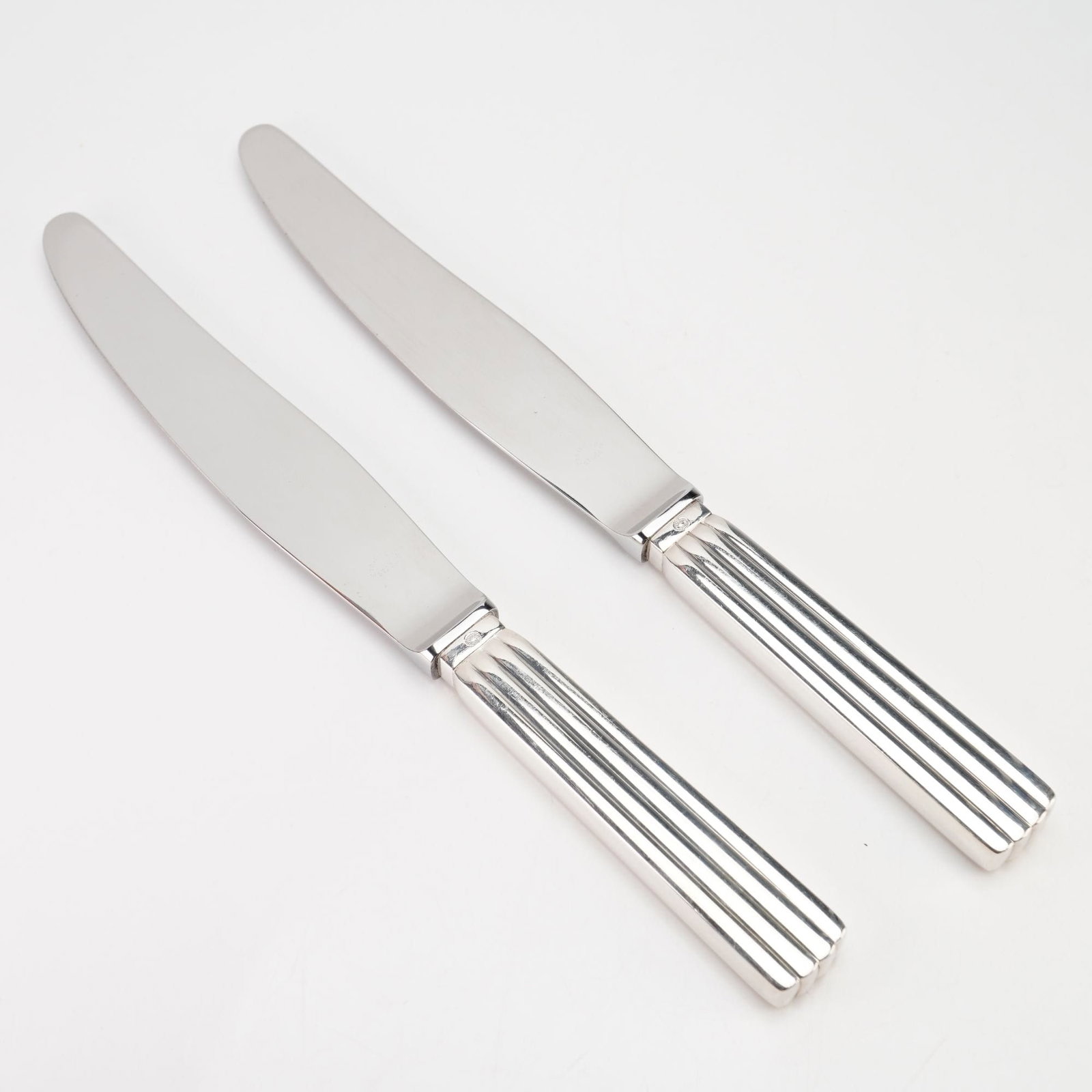 Georg Jensen, Bernadotte, A Pair of Dinner Knives, Sterling Silver Handles: A pair of dinner knives in the Bernadotte pattern, designed by Sigvard Bernadotte for Georg Jensen. These pieces feature sterling silver handles with vertical fluting and stainless steel blades. The h