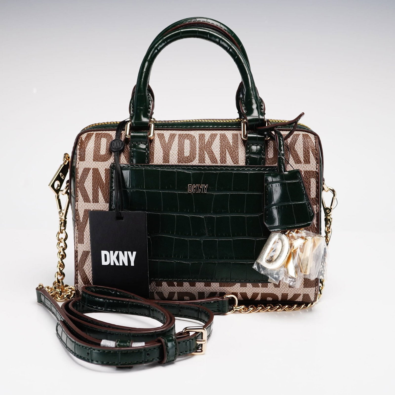 DKNY Paige Mini Monogram Duffle Bag: The DKNY Paige mini monogram duffle bag is a compact, versatile accessory. It features a classic monogram pattern and is constructed with a durable soft-shell finish. The interior includes multiple co
