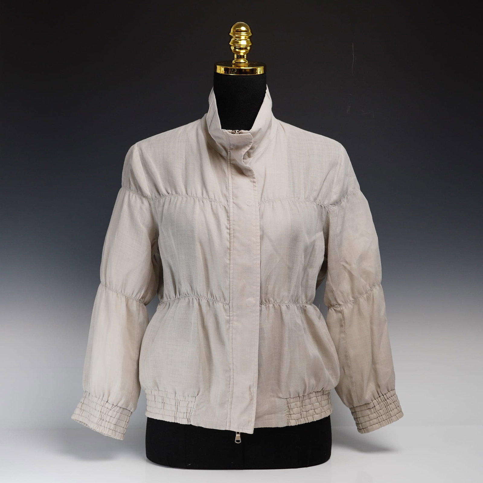 Brunello Cucinelli Ruffled Spring Jacket: This Brunello Cucinelli ruffled spring jacket is crafted from a sand-colored lightweight woven fabric with a subtle sheen. The contemporary design features horizontal tiered stitching across the chest