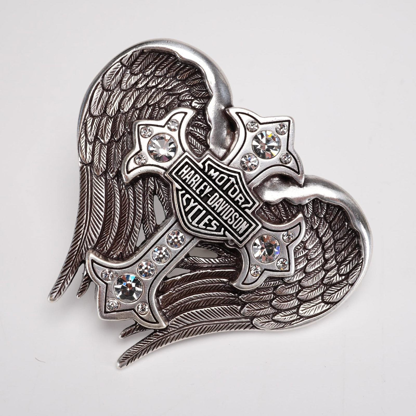 Harley-Davidson Back Roads Cross Winged Belt Buckle: This silver-tone Harley-Davidson belt buckle consists of a cross embellished with clear, faceted rhinestones, with the iconic Bar and Shield logo set at the center. The cross is framed by two large, d