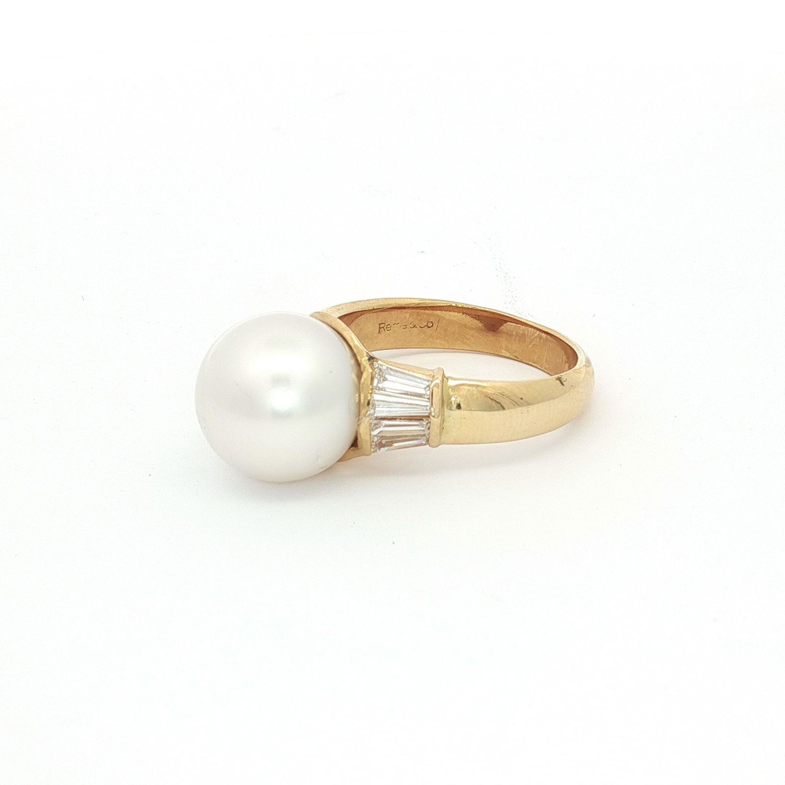 18K Yellow Gold Ring with Round White Pearl and Baguette Diamonds: An estate ring crafted in 18K yellow gold. The ring features a large, round white pearl center stone secured in a raised mounting. Flanking the center stone on each shoulder are several channel-set, b