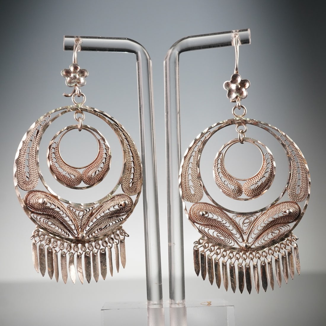 Pair of Sterling Silver Filigree Drop Earrings: A pair of sterling silver circular drop earrings featuring layered openwork filigree elements, with an outer hammered hoop enclosing a smaller suspended ring, both decorated with delicate scroll and f