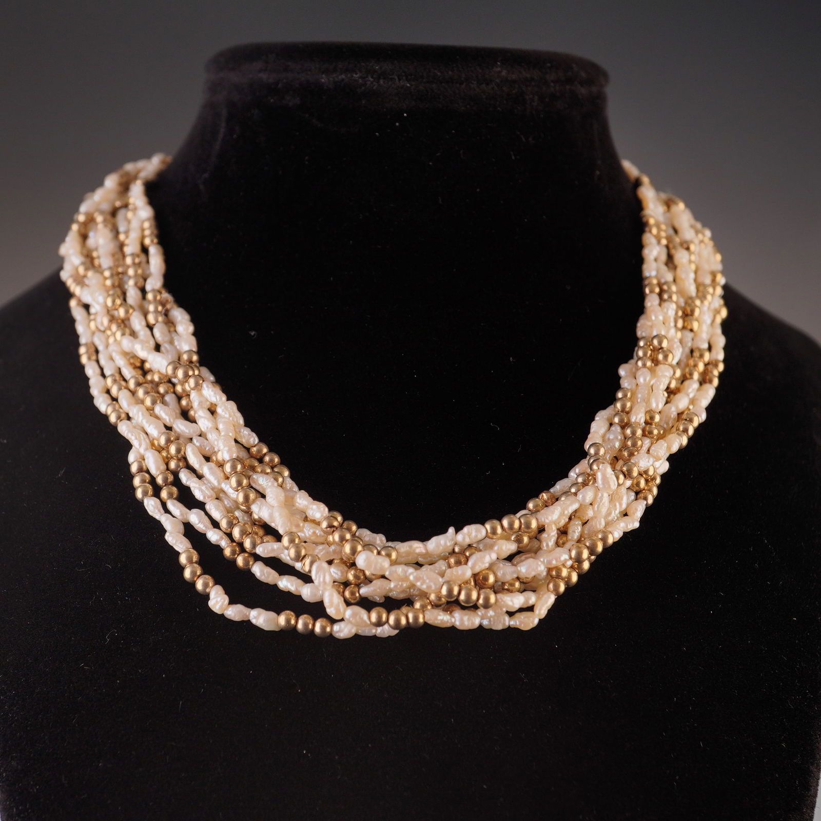 Italian 18K Gold Multi Strand Rice Pearl Necklace: A ten-strand necklace crafted from segments of rice pearls interspersed with gold beads. The necklace features a gold push-in clasp with a twist pattern, marked 750 and bearing Italian hallmarks. Dime