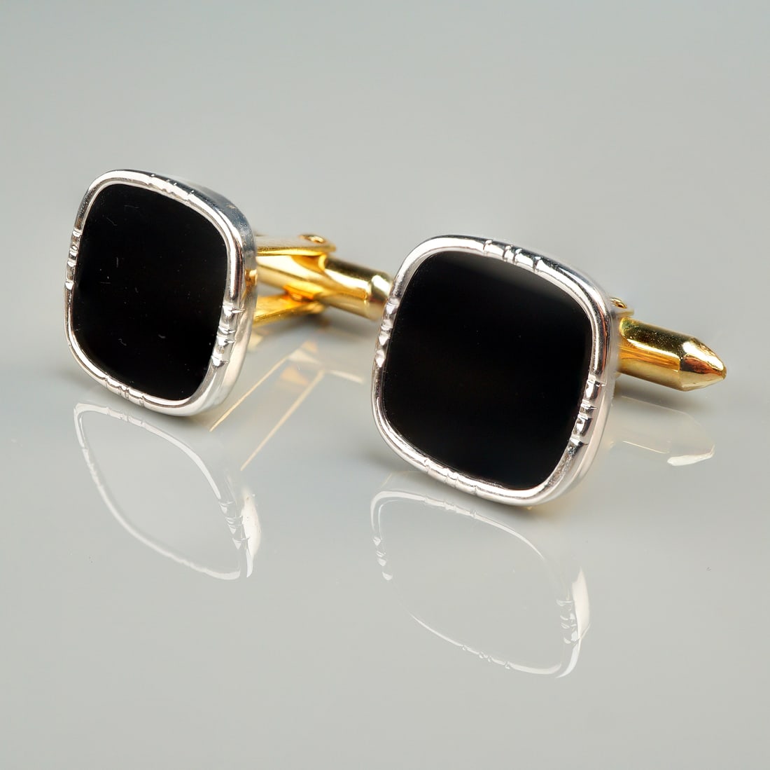 A Pair of 14K Gold-Toned and Black Inlaid Cushion Cufflinks: A pair of men's cufflinks featuring a classic dual-tone construction. The faces are cushion-shaped, inlaid with a polished, solid black material, likely onyx or black enamel. The inlay is secured by a