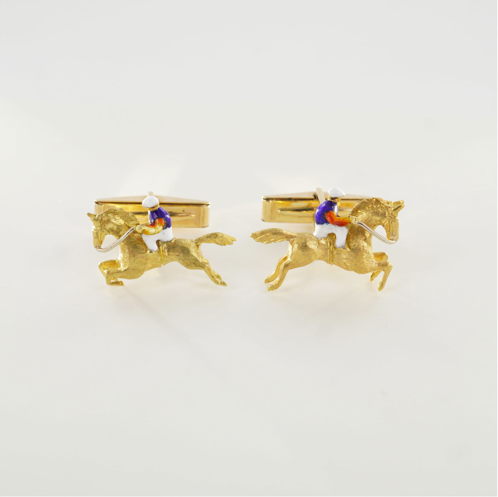 Pair of 14K Yellow Gold Horse and Jockey Cufflinks: Finely crafted pair of 14K yellow gold cufflinks depicting a horse and jockey mid-gallop, accented with colorful hand-applied enamel. The figures display excellent detail and motion, capturing the ene