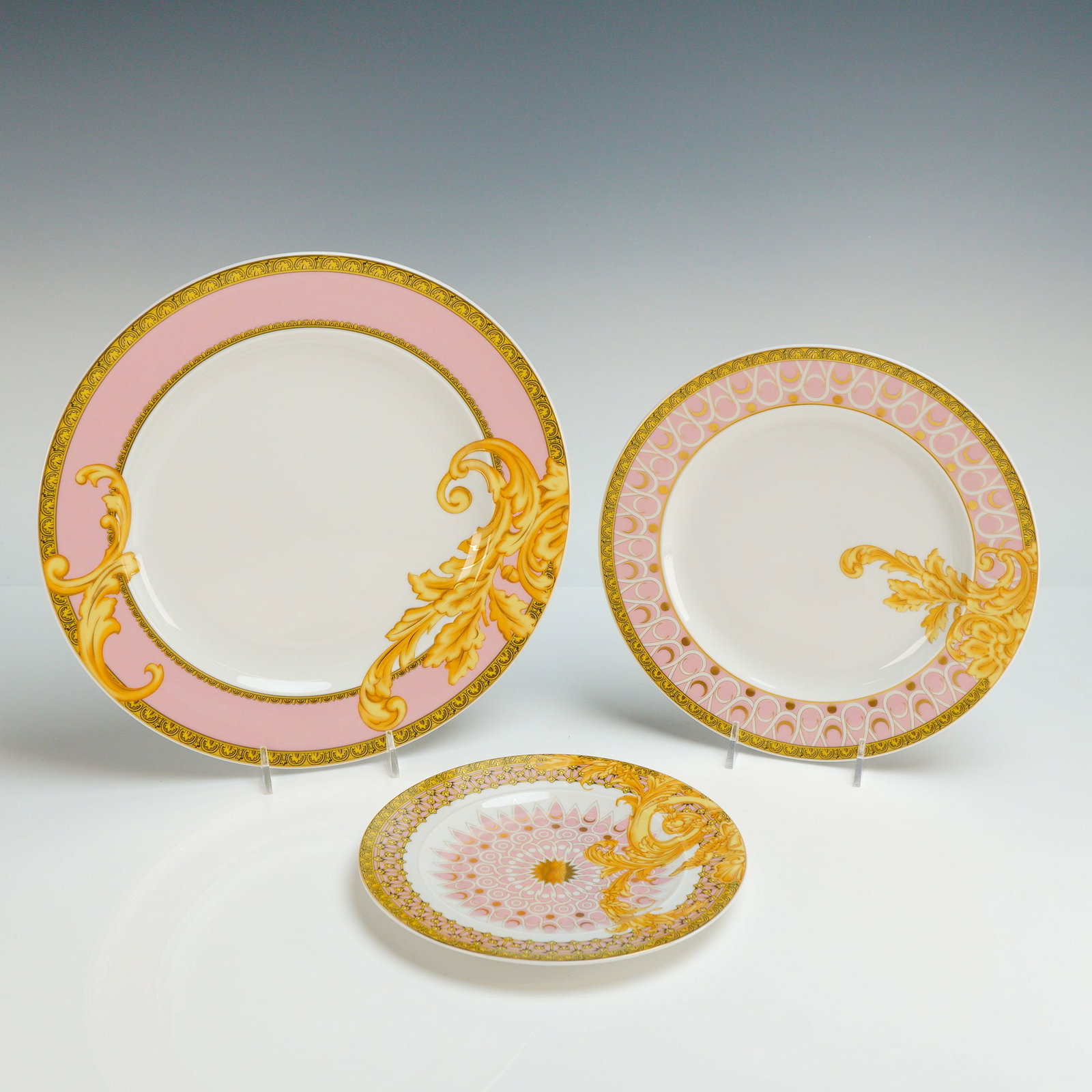 3pc Versace Rosenthal Porcelain Plate Set, Les Reves Byzantins: The graduated pieces feature a palette of pink, white, and gold, decorated with characteristic Barocco acanthus leaf scrolls, intricate geometric lattice patterns, and classical scroll borders. The sm