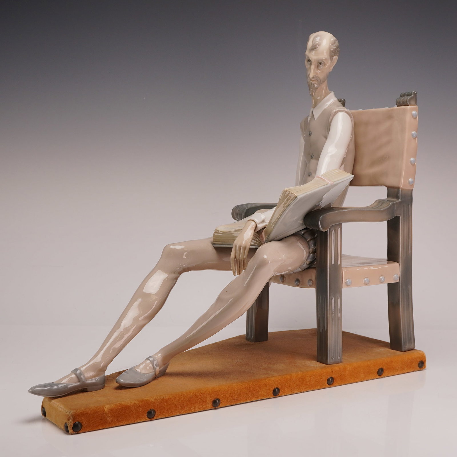 Lladro Don Quixote Porcelain Figurine Model 01001030 with Base: This Lladro porcelain figurine, model number 01001030, depicts the character Don Quixote seated in a high-backed armchair. The figure is captured in a moment of reflection, reading an open book while