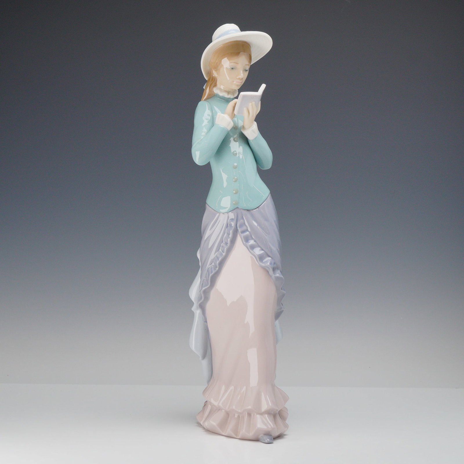 Lladro Glazed Porcelain Figurine, Reading 1005000: A Lladro glazed porcelain figurine titled Reading, model number 5000, sculpted by Francisco Catala and first issued in 1978. The figure depicts a young woman in elegant late 19th-century attire, stand
