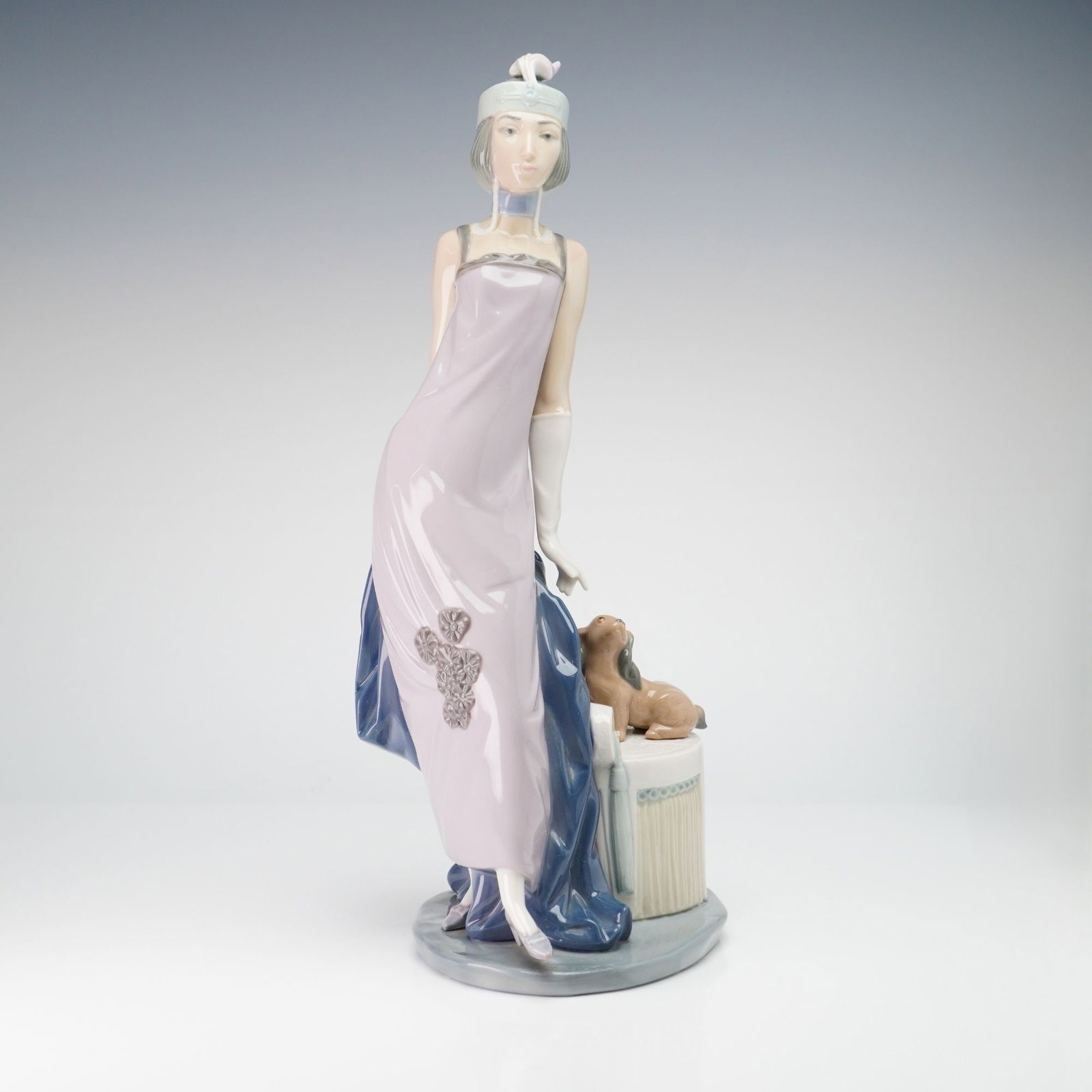 Lladro Porcelain Figurine Couplet Lady 01005174: A Lladro glazed porcelain figurine titled Couplet Lady, model number 01005174. The piece depicts a woman in a 1920s style ensemble, featuring a floor-length sleeveless lilac gown with molded floral cl