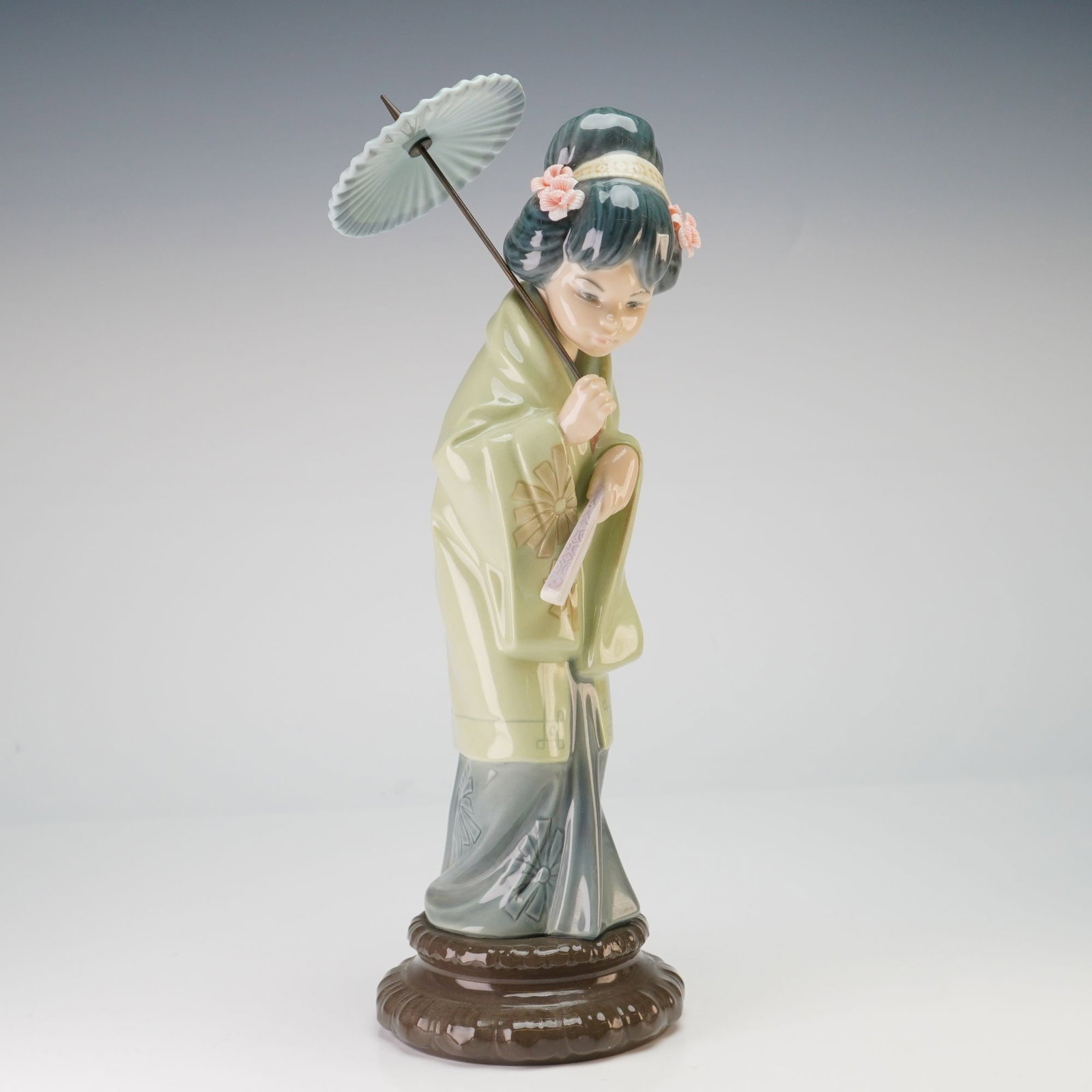 Lladro Porcelain Figurine, Oriental Spring 4988: A young Japanese woman in traditional attire. The figure is depicted in a graceful, slightly bowed pose wearing a pale sage-green kimono featuring a large stylized floral motif, worn over a darker gra