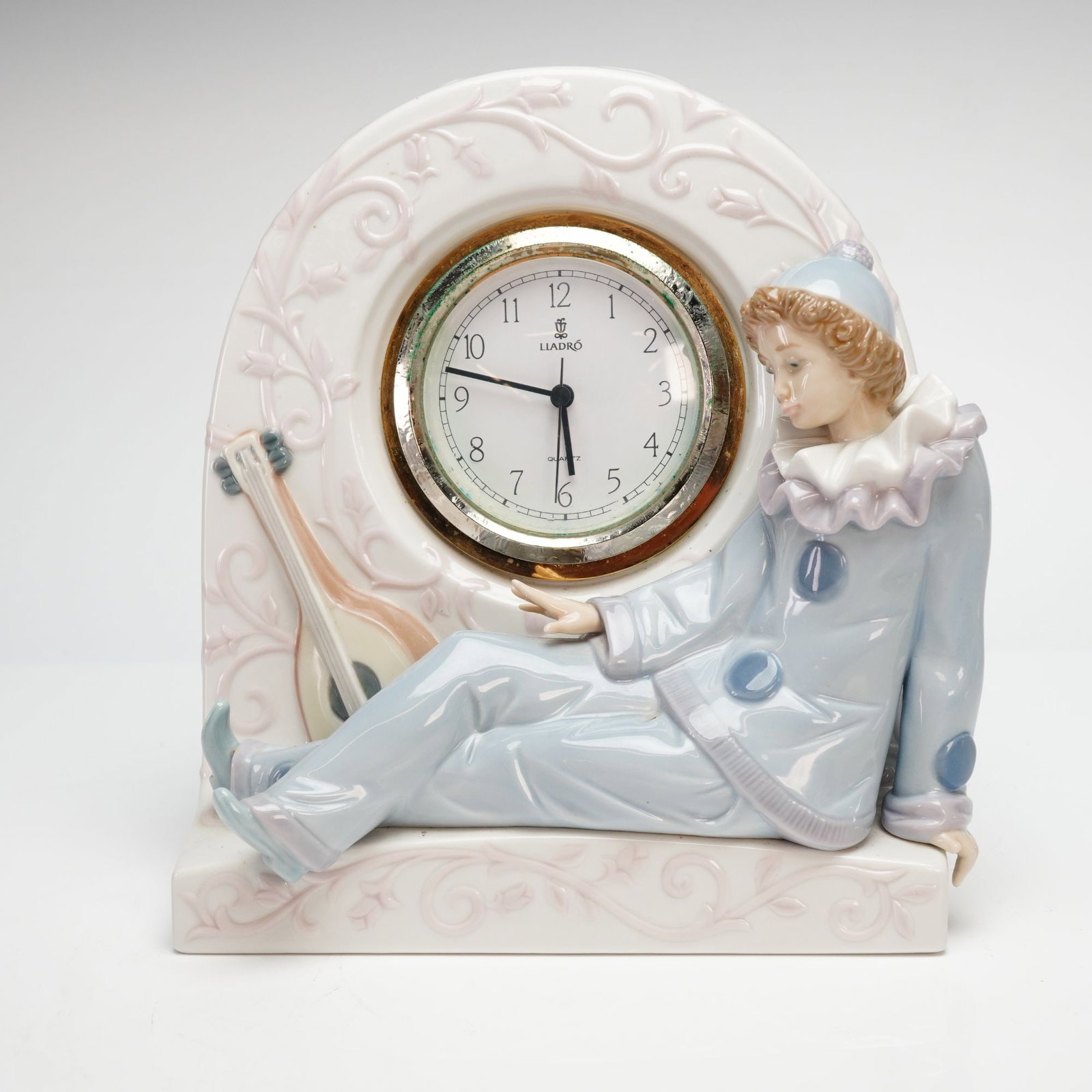 Lladro Porcelain Mantel Clock, Pierrot 1005778: A fine glazed porcelain mantel clock manufactured by Lladro in Spain, model number 5778, titled Pierrot Clock. The piece features a seated Pierrot figurine in a pale blue and lavender outfit resting a