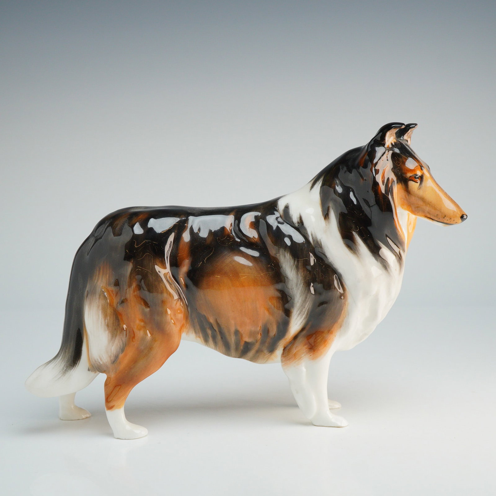 Royal Doulton Figurine, Collie HN1058: Royal Doulton designed by Frederick Daws. This glazed ceramic figure is modeled in a standing pose with a tri-color coat of black, white, and tan. The piece is finished with a high-gloss glaze. The un