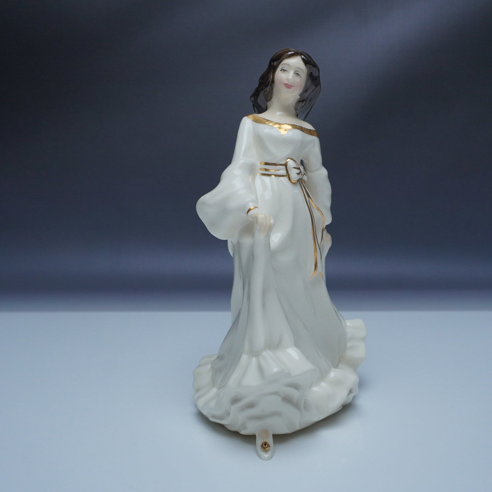 Royal Doulton Figurine, Free Spirit HN3728: This Royal Doulton figurine, titled "Free Spirit" (HN3728), depicts a graceful woman in flowing white attire with gold accents and a soft, serene expression. Sculpted by artist Margaret Tarrant, this