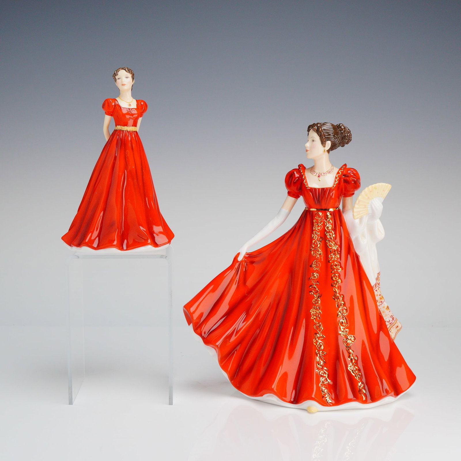 Royal Doulton Figurines 200th Anniversary Set, Eleanor and Ellie: The figures depict women wearing dramatic, high-waisted ball gowns rendered in a deep glossy red glaze accented with gold luster detailing. The larger figure, Eleanor, is marked HN 5725 and identified