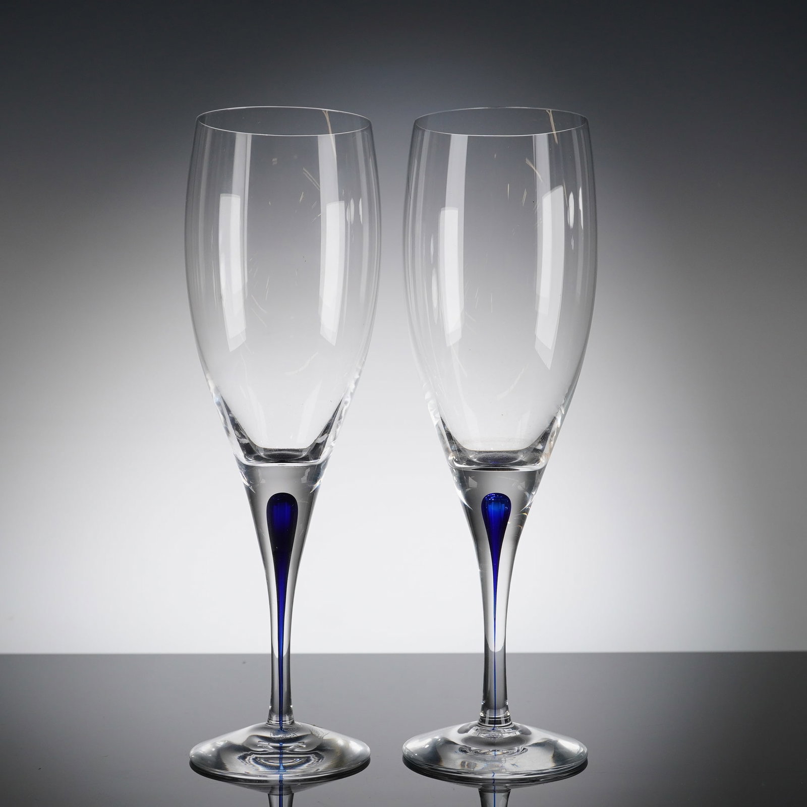 A Pair of Orrefors Intermezzo Blue Crystal Champagne Flutes: A pair of Orrefors Intermezzo Blue crystal champagne ?utes. These 2pc Orrefors Crystal intermezzo blue glasses feature tall, slender bowls atop clear stems. The design is characterized by a striking i