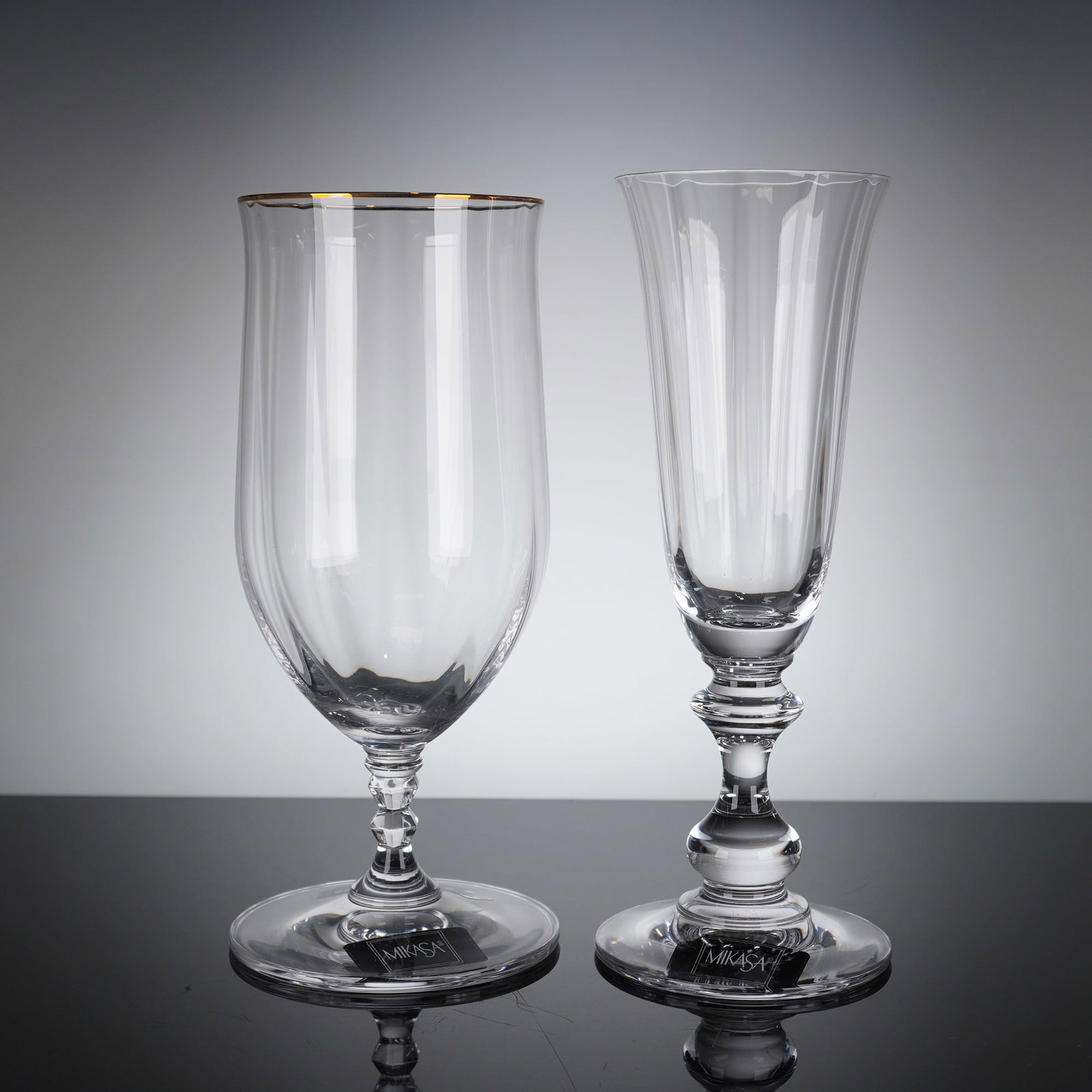 2pc Mikasa Crystal Iced Tea and Champgane Glasses: A group of Mikasa crystal stemware items consisting of one iced tea glass in the Sonata Gold pattern and one champagne flute in the French Countryside pattern. Both pieces are crafted from clear cryst