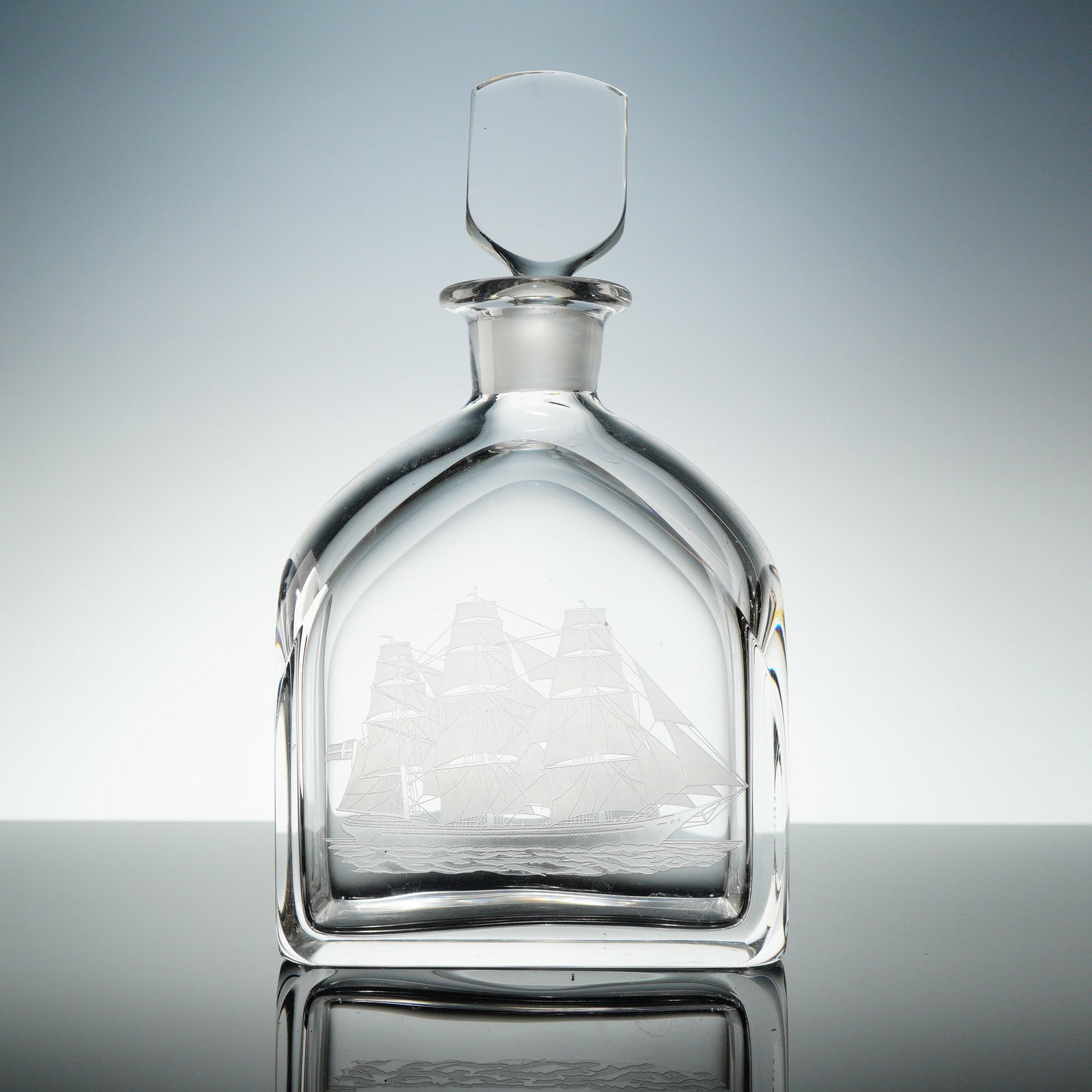 Orrefors Engraved Ship Motif Crystal Decanter with Stopper: A heavy, clear Orrefors crystal decanter with stopper, atributed to Edward Hald. The lot consists of two items: the decanter vessel and its matching faceted shield-shaped stopper. The decanter feature