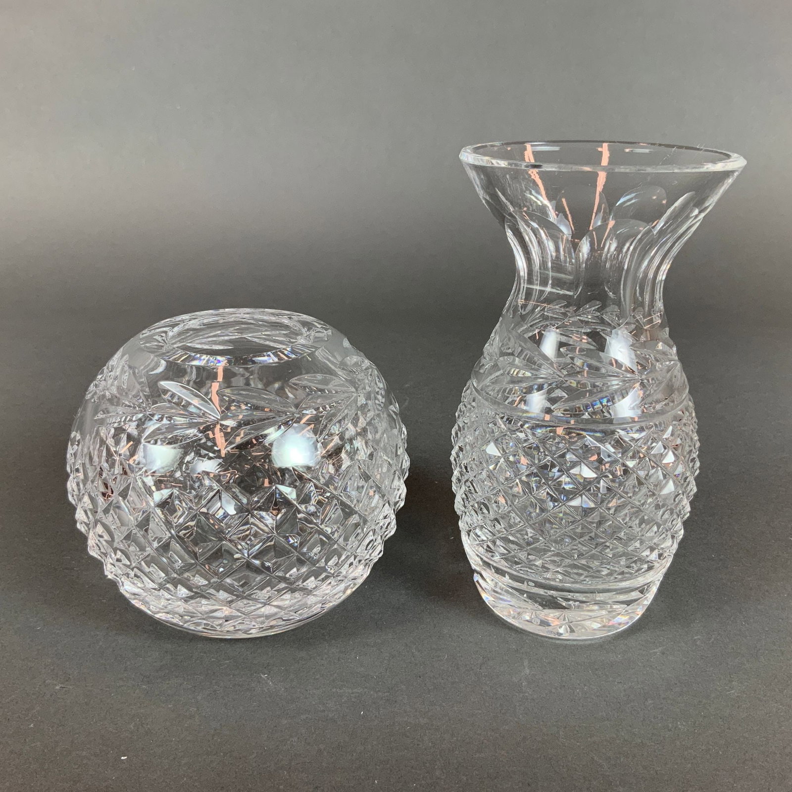 Two Waterford Crystal Glandore Round and Tall Vases: A pair of Waterford lead crystal vessels in the Glandore pattern, manufactured in Ireland. The first item is a globular rose bowl featuring a wide circular opening. The exterior is decorated with a pr