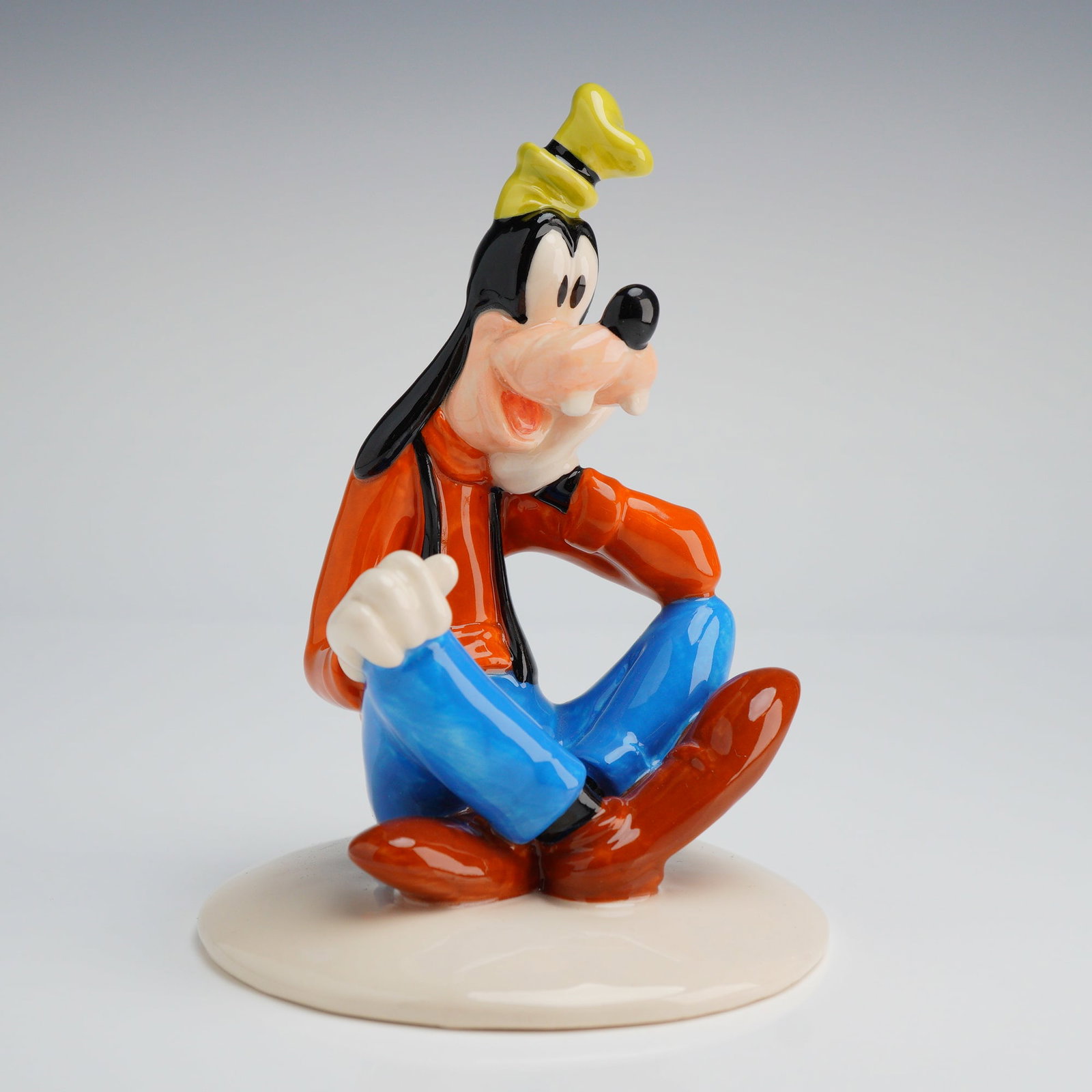Royal Doulton Mickey Mouse Collection Goofy NM5 Figurine with Box: A glazed ceramic figurine depicting the Walt Disney character Goofy, produced by Royal Doulton as part of The Mickey Mouse Collection. The figure is modeled seated with crossed legs, executed in brigh