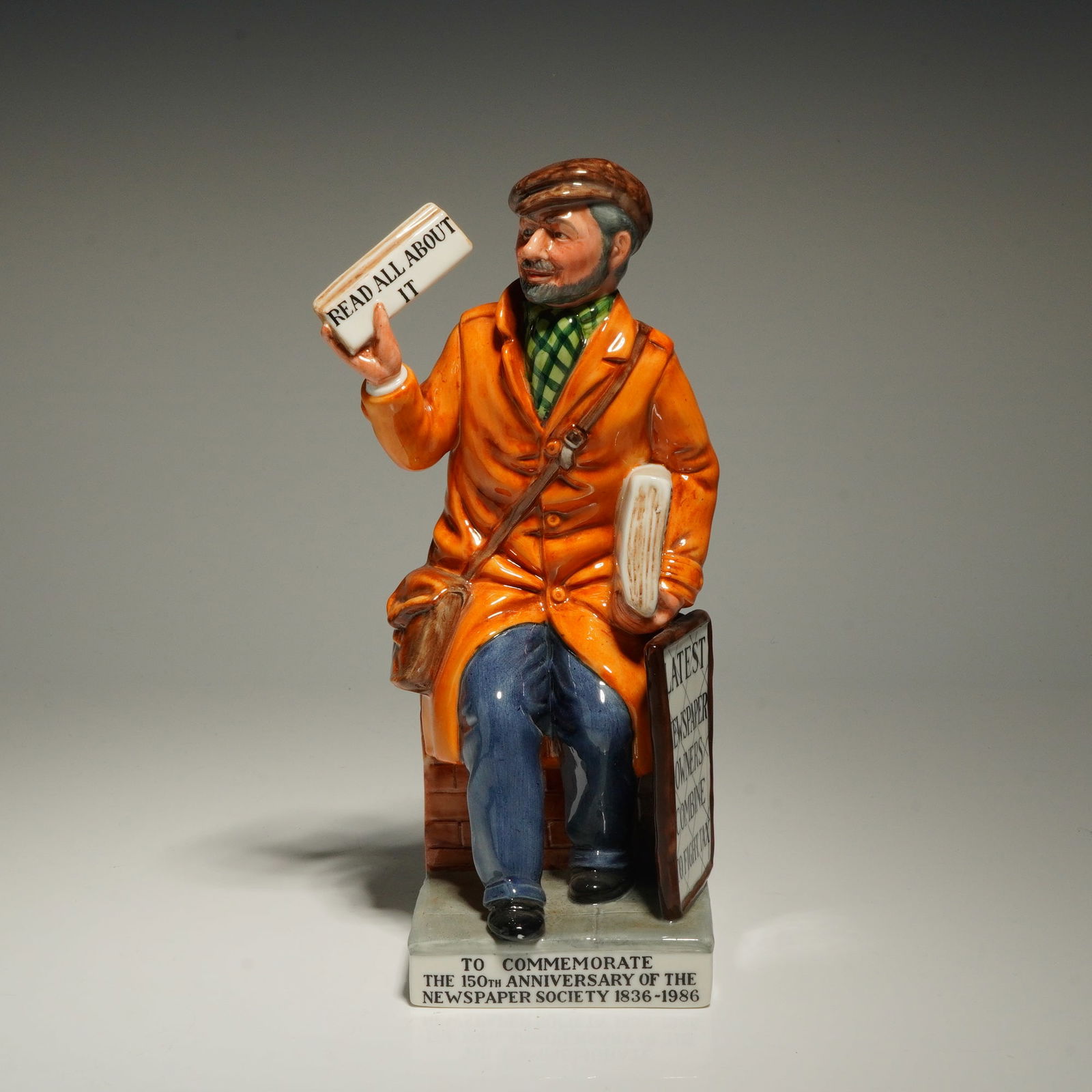 Royal Doulton Figurine, The Newsvendor HN2891: A Royal Doulton ceramic figurine titled The Newsvendor, model HN 2891, modeled by William K. Harper and dated 1985. The hand-painted figure depicts a man in a flat cap and orange overcoat seated on a