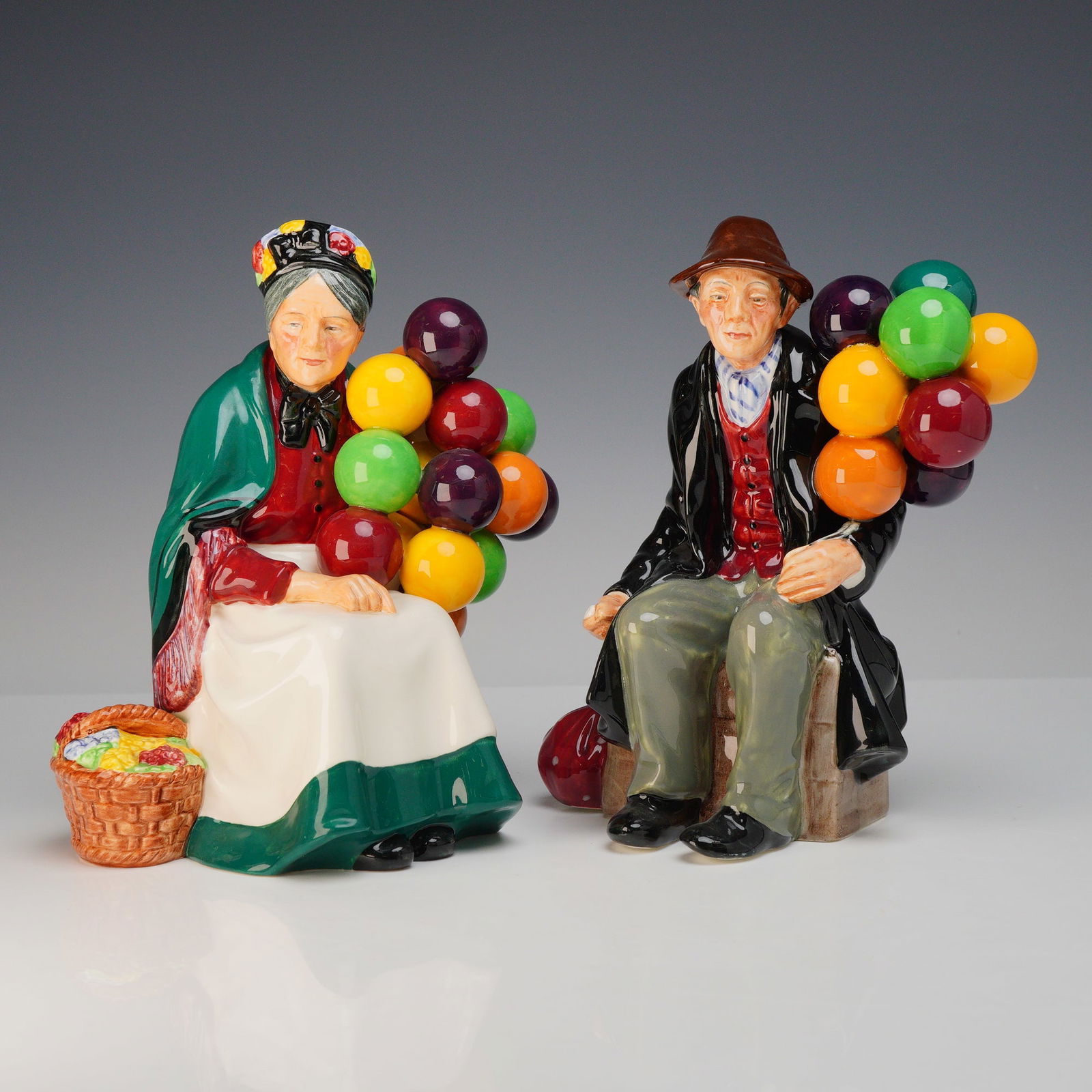 2pc Royal Doulton Figurines, The Old Balloon Seller and The Balloon Man: This lot features a pair of 2 rdf (Royal Doulton figurines) from the classic Balloon character series. The first figurine is The Old Balloon Seller, model HN1315, which depicts an elderly woman in a f