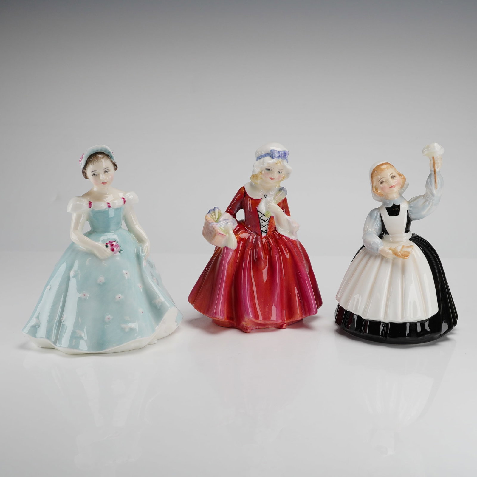 3pc Royal Doulton Porcelain Figurines: This trio of Royal Doulton bone china figurines features hand-painted female characters in historical and traditional attire. The collection includes The Bridesmaid HN2196 depicted in a pale blue flor