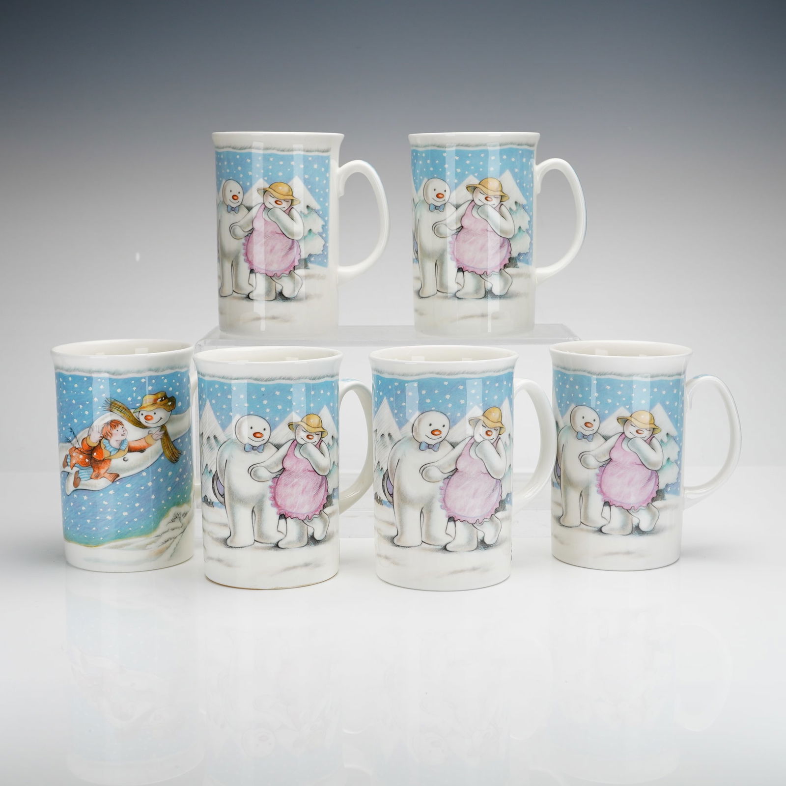 6pc Royal Doulton The Snowman Gift Collection, The Party Mugs: A collection of six Royal Doulton ceramic mugs from The Snowman Gift Collection, featuring The Party pattern. The pieces are made of white glazed ceramic with transfer-printed illustrations based on c