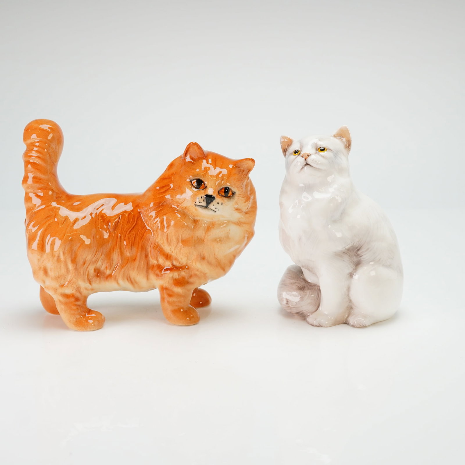 Two Royal Doulton Persian Cat Figurines, DA132 & HN2539: A pair of Royal Doulton glazed bone china figurines depicting Persian cats. The collection includes one ginger Persian cat, identified as model DA132, and one white Persian cat, identified as model HN