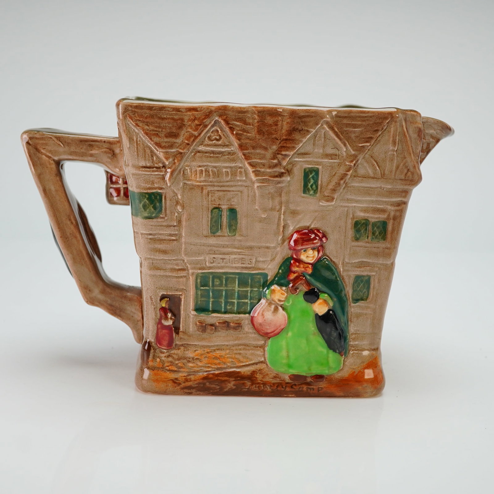 Royal Doulton Dickensware Pitcher, Old London: The item features a rectangular tapering form with relief-molded polychrome decoration. One side depicts the character Sairey Gamp in a green dress and red hood before a Tudor-style building with a si