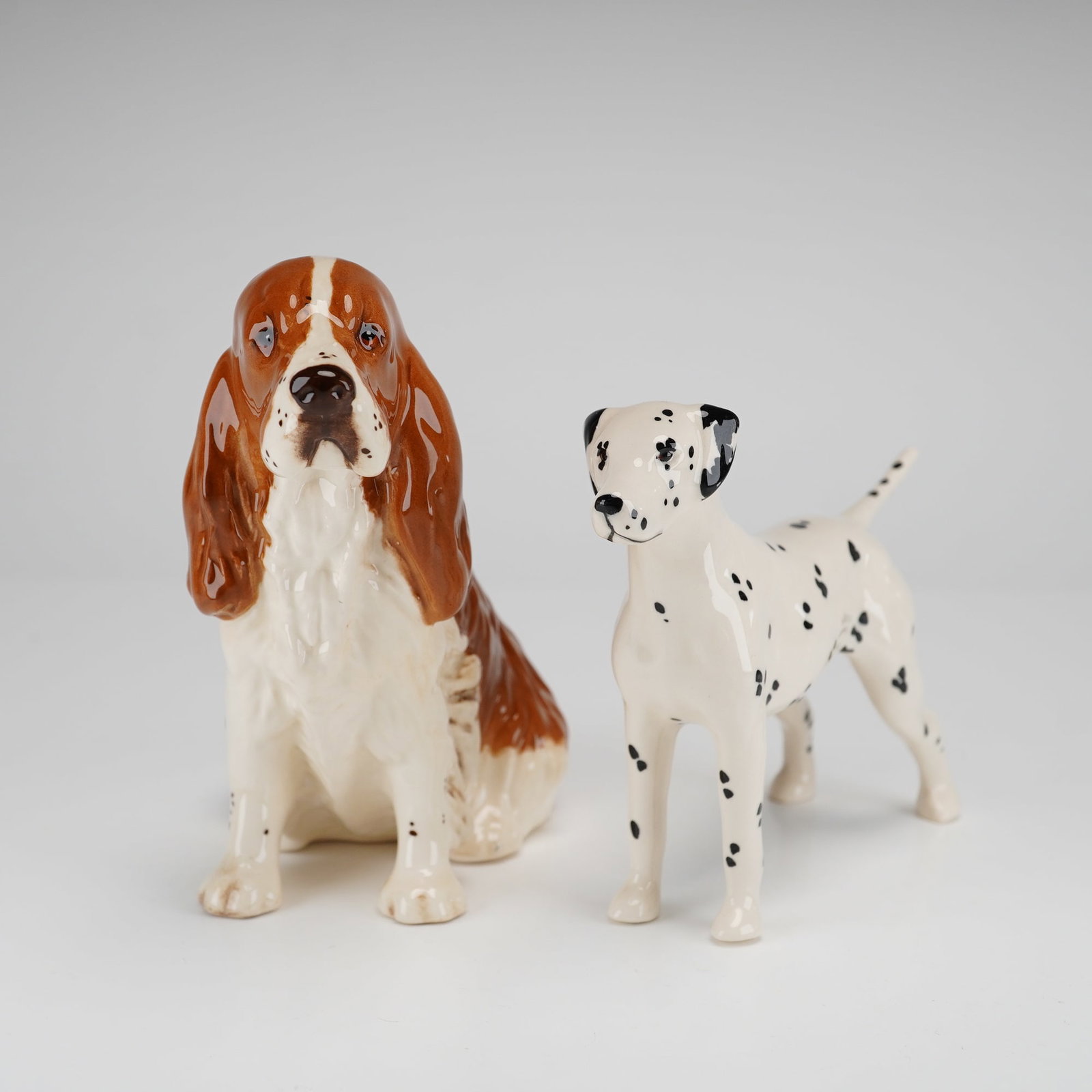 2pc Royal Doulton & Beswick Figurines, Cocker Spaniel & Dalmatian: The Royal Doulton figurine depicts a seated Cocker Spaniel in a liver and white color scheme, identified as model HN1037. It bears the Royal Doulton lion and crown backstamp on the underside accompani