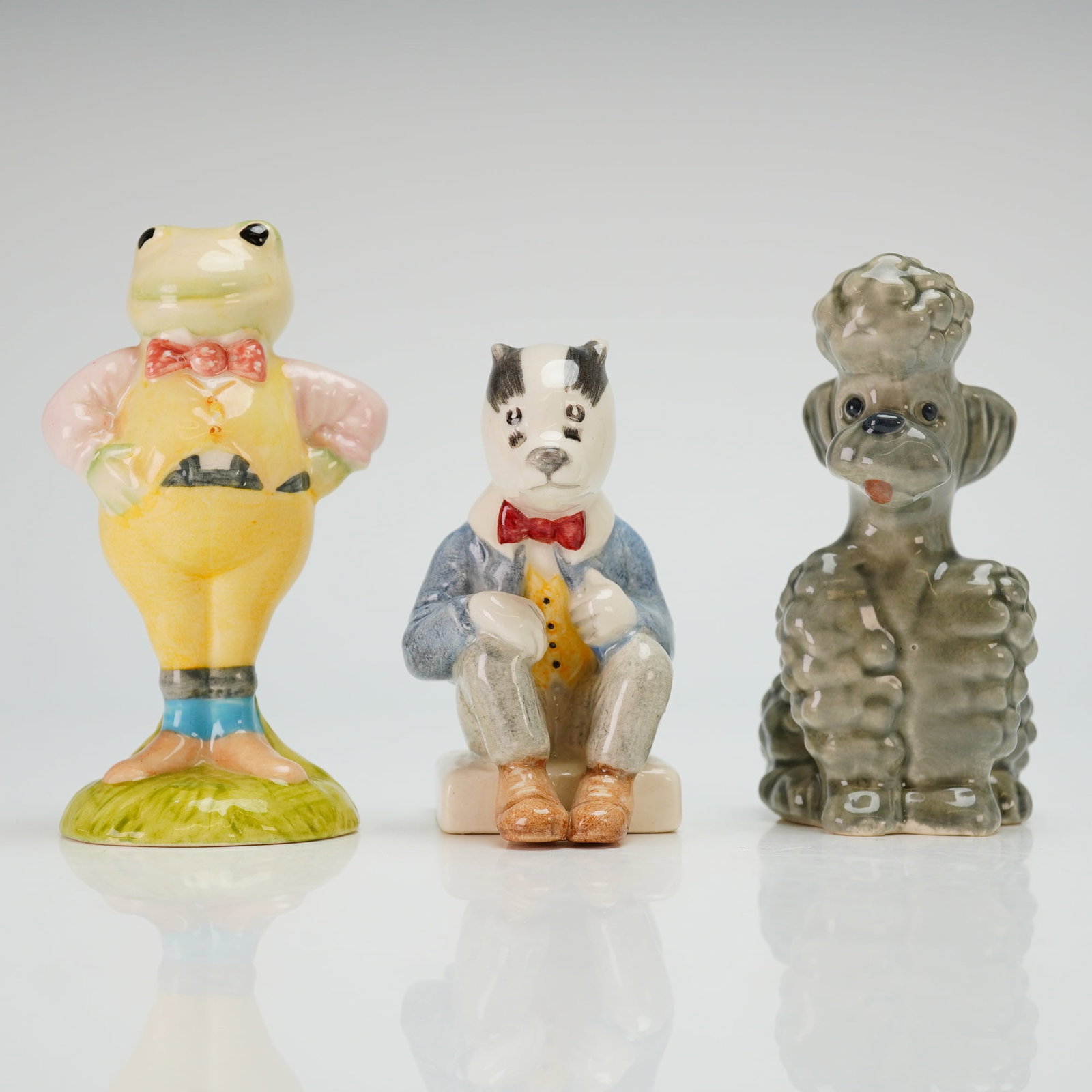 Three Figurines by Royal Albert Toad, Beswick Bill Badger & Goebel Poodle: The Royal Albert Toad figurine from The Wind in the Willows series is dated 1987 and features an anthropomorphic toad in a yellow suit, pink shirt, and red bow tie. The Beswick Bill Badger figurine fr