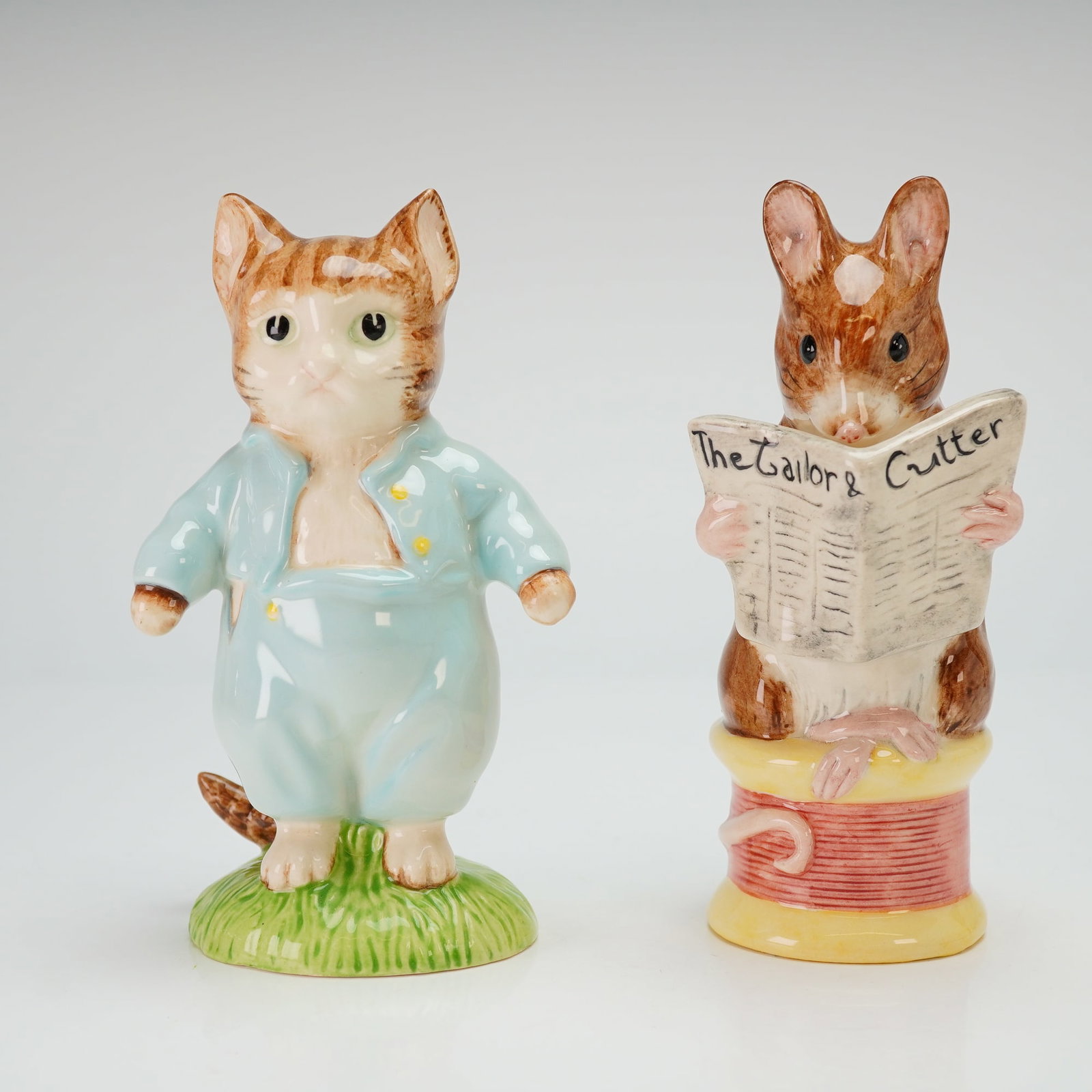 Two Royal Albert Beatrix Potter Figurines, Tom Kitten and The Tailor: Two figurines based on the literary characters of Beatrix Potter, featuring a large size Tom Kitten and The Tailor of Gloucester. The Tom Kitten figurine depicts a ginger cat wearing a light blue suit