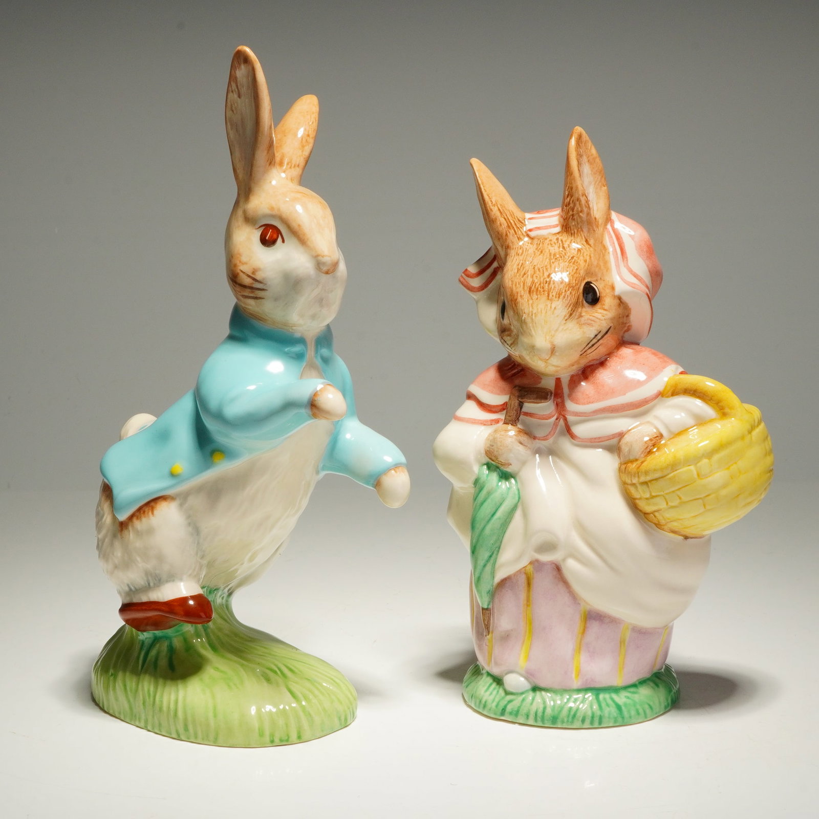 2pc Royal Albert Beatrix Potter Large Figurines, Peter Rabbit & Mrs. Rabbit: A pair of Royal Albert porcelain figurines from the Beatrix Potter collection, featuring the characters Peter Rabbit and Mrs. Rabbit. Peter Rabbit is modeled in his signature blue jacket, standing on