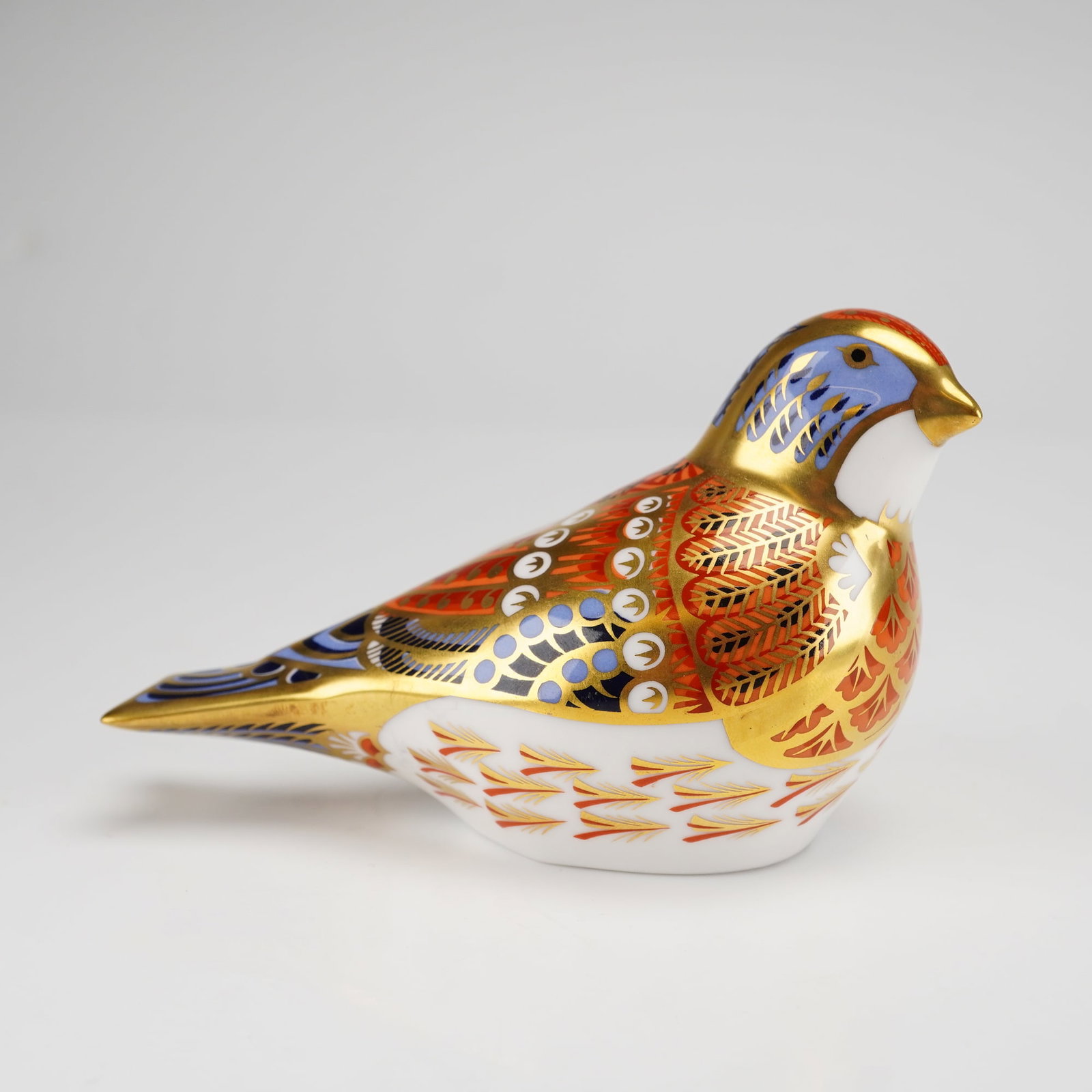 Royal Crown Derby Linnet Porcelain Paperweight: A Royal Crown Derby porcelain paperweight titled Linnet, featuring a stylized bird form decorated in an Imari-style palette of cobalt blue, iron red, and orange, accented with gold gilding. Designed b